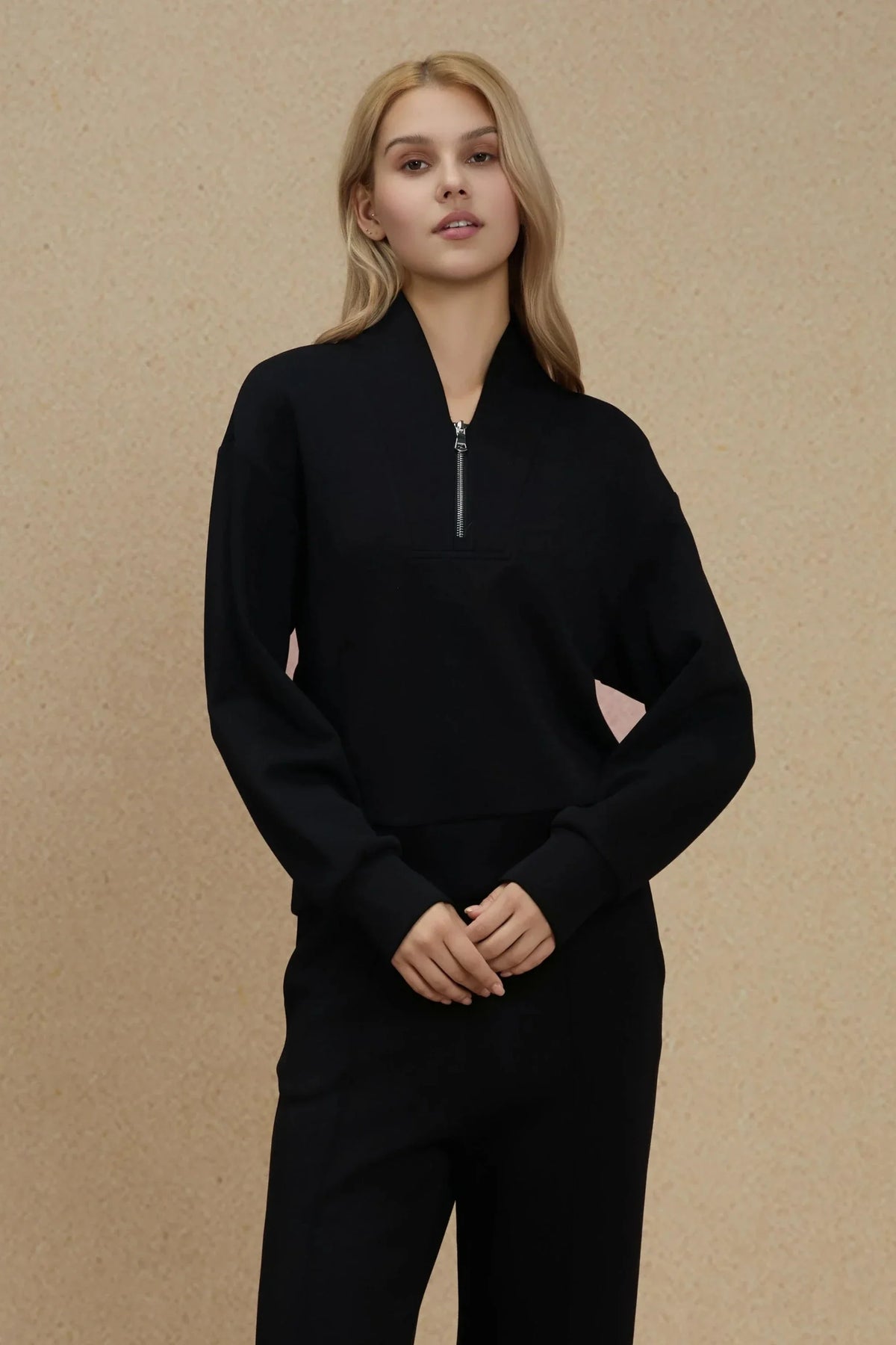 Woman standing in an Onyx Black half-zip golf pullover with matching pants, showing the relaxed silhouette