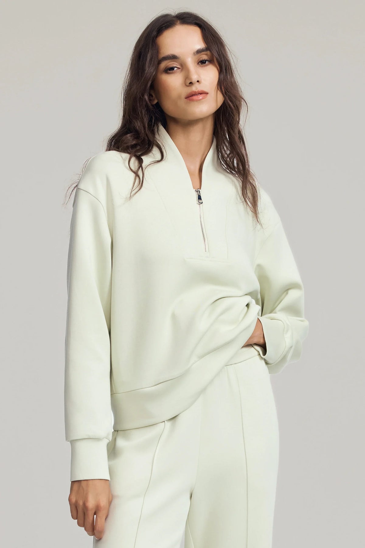 Woman wearing a Pistachio Cream half-zip golf pullover with a soft stand collar, relaxed fit and matching pants
