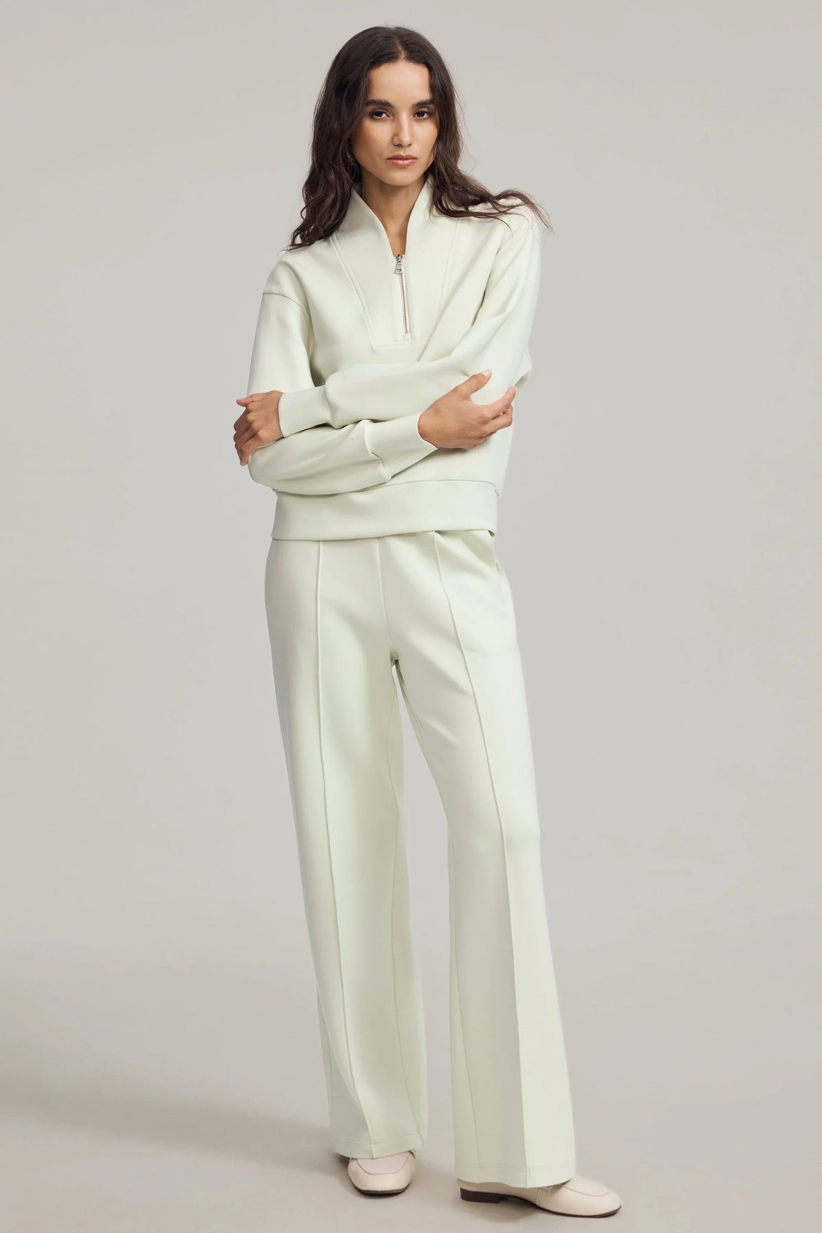 Woman standing in a Pistachio Cream half-zip golf pullover and matching pants, showing the relaxed silhouette and half-zip neckline