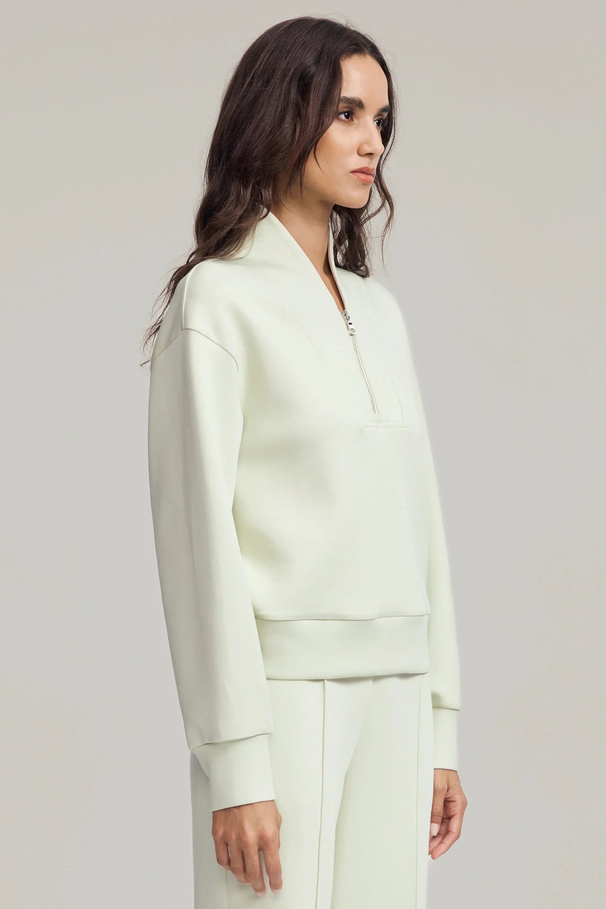 Side view of women's light cream half-zip golf pullover showing dropped shoulders, relaxed sleeves and matching fabric hem