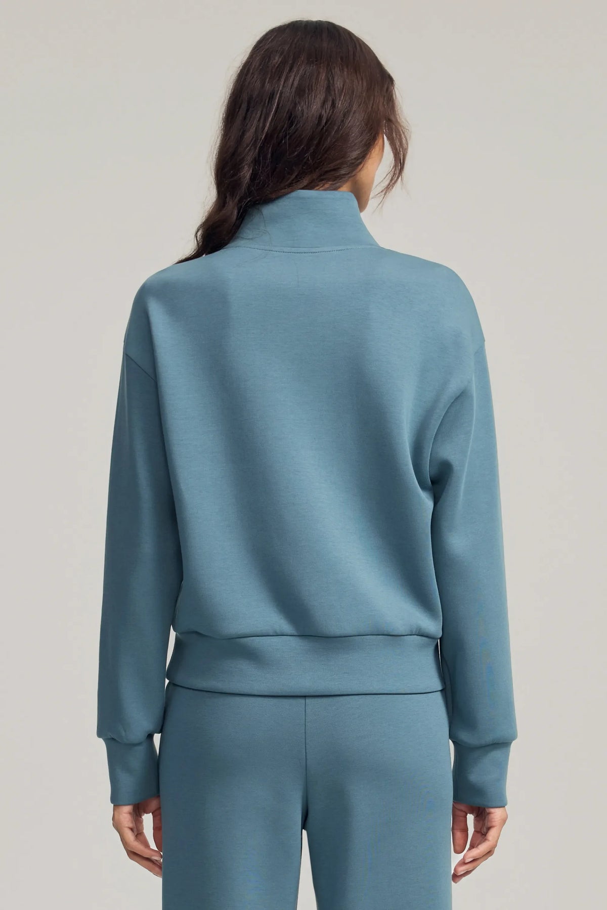 Back view of women's blue half-zip golf pullover showing dropped shoulders, relaxed sleeves and matching fabric hem