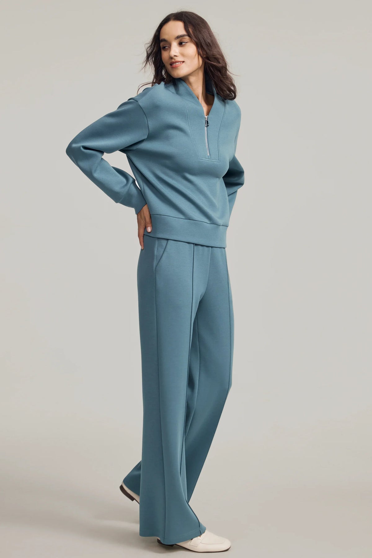 Woman wearing a Slate Blue half-zip golf pullover with matching straight-leg pants in a relaxed side pose