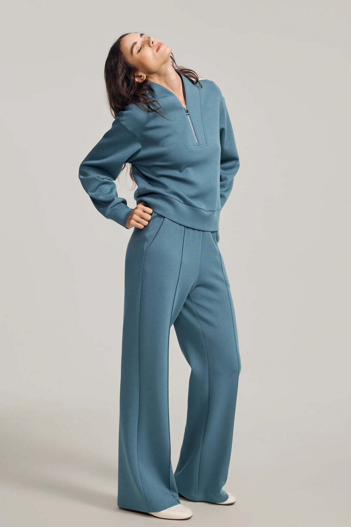 Woman posing with one hand on her hip in a blue half-zip golf pullover and matching straight-leg pants