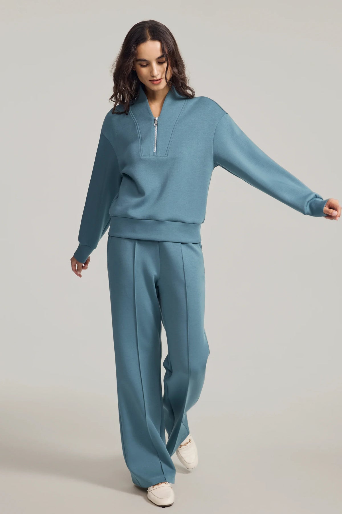 Woman walking in a blue half-zip golf pullover and matching straight-leg pants, showing the relaxed silhouette in motion