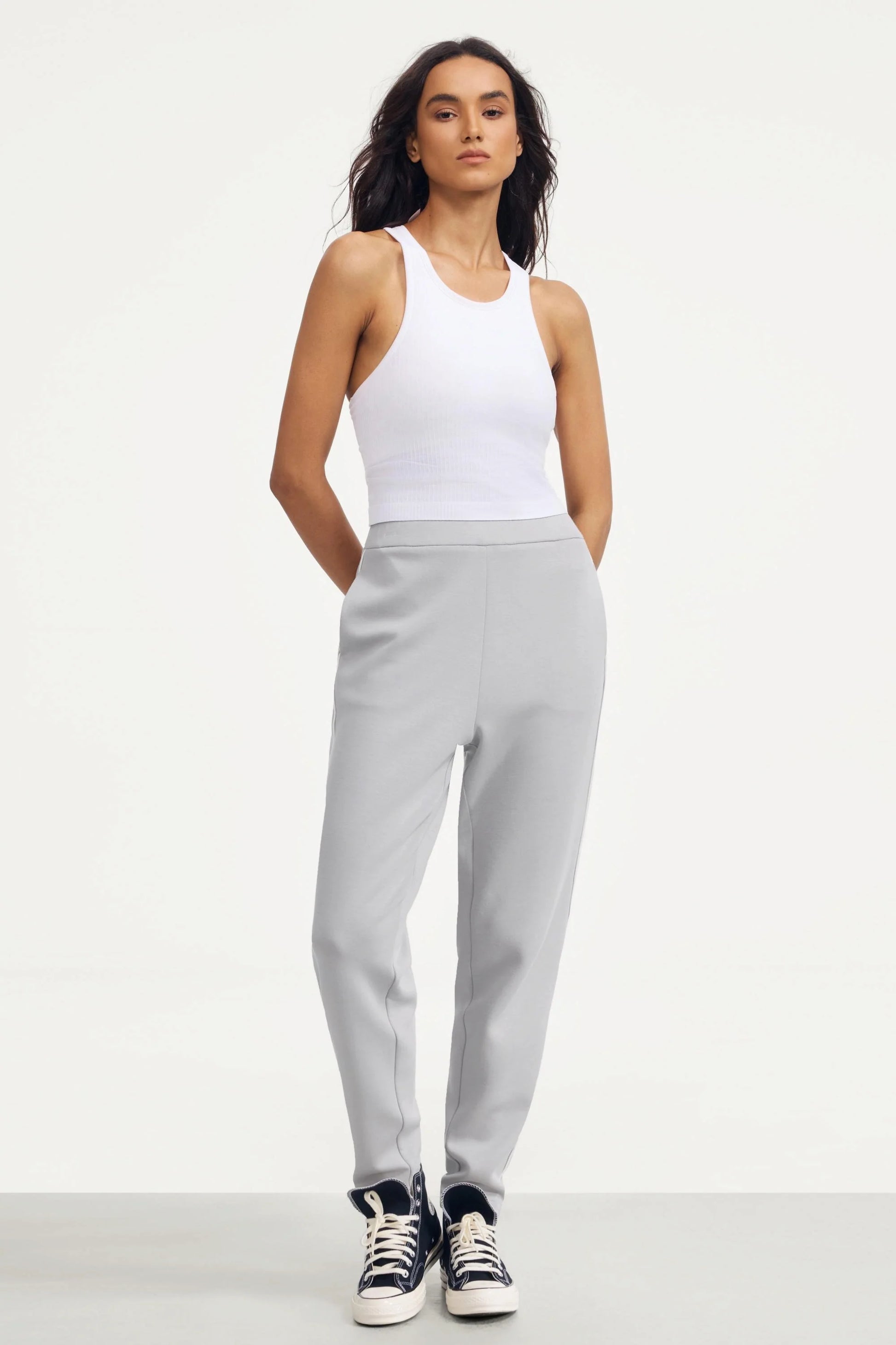 Woman wearing Soft Cloud Grey track pants styled with a white fitted tank top