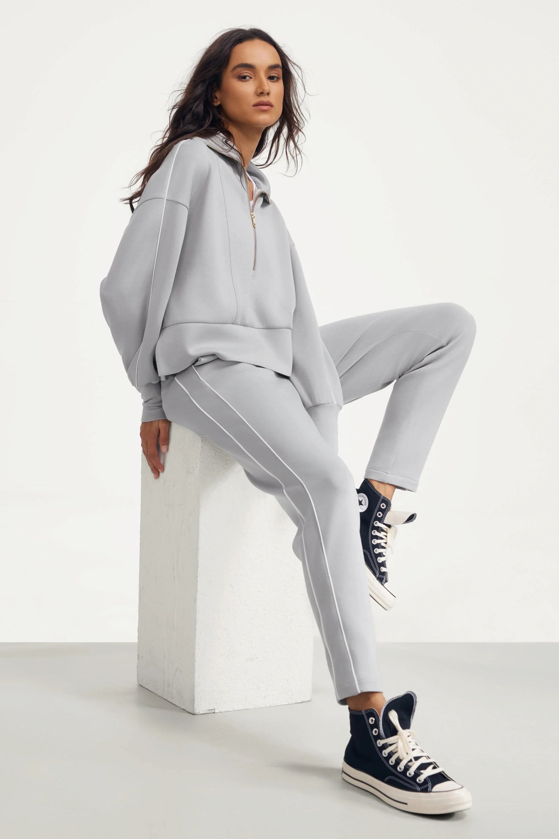 Woman wearing Soft Cloud Grey slim fit track pants styled with a matching half-zip top in a seated look