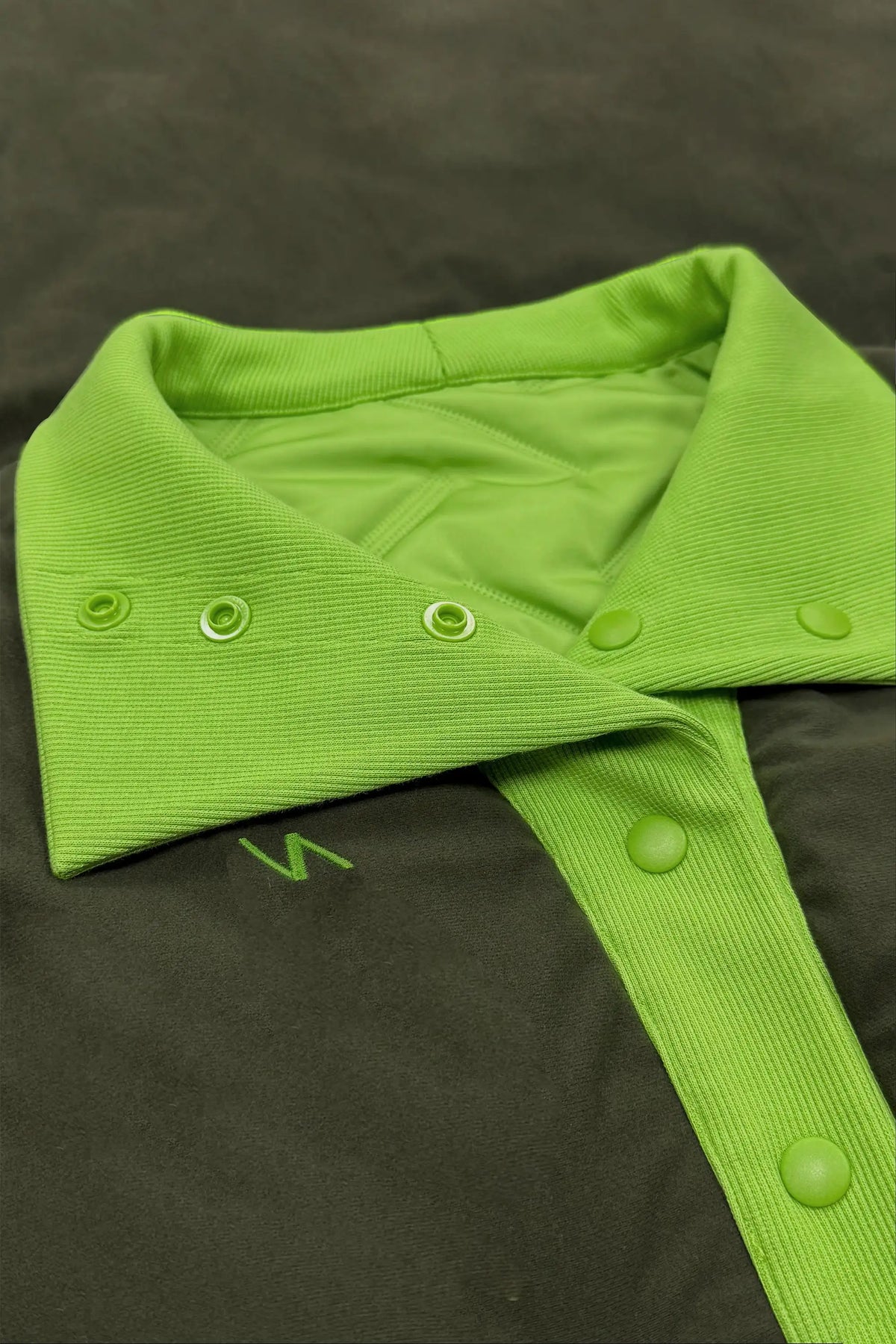 Close-up of reversible women’s lightweight puffer vest with dark reverse side, bright green ribbed collar and embroidered logo