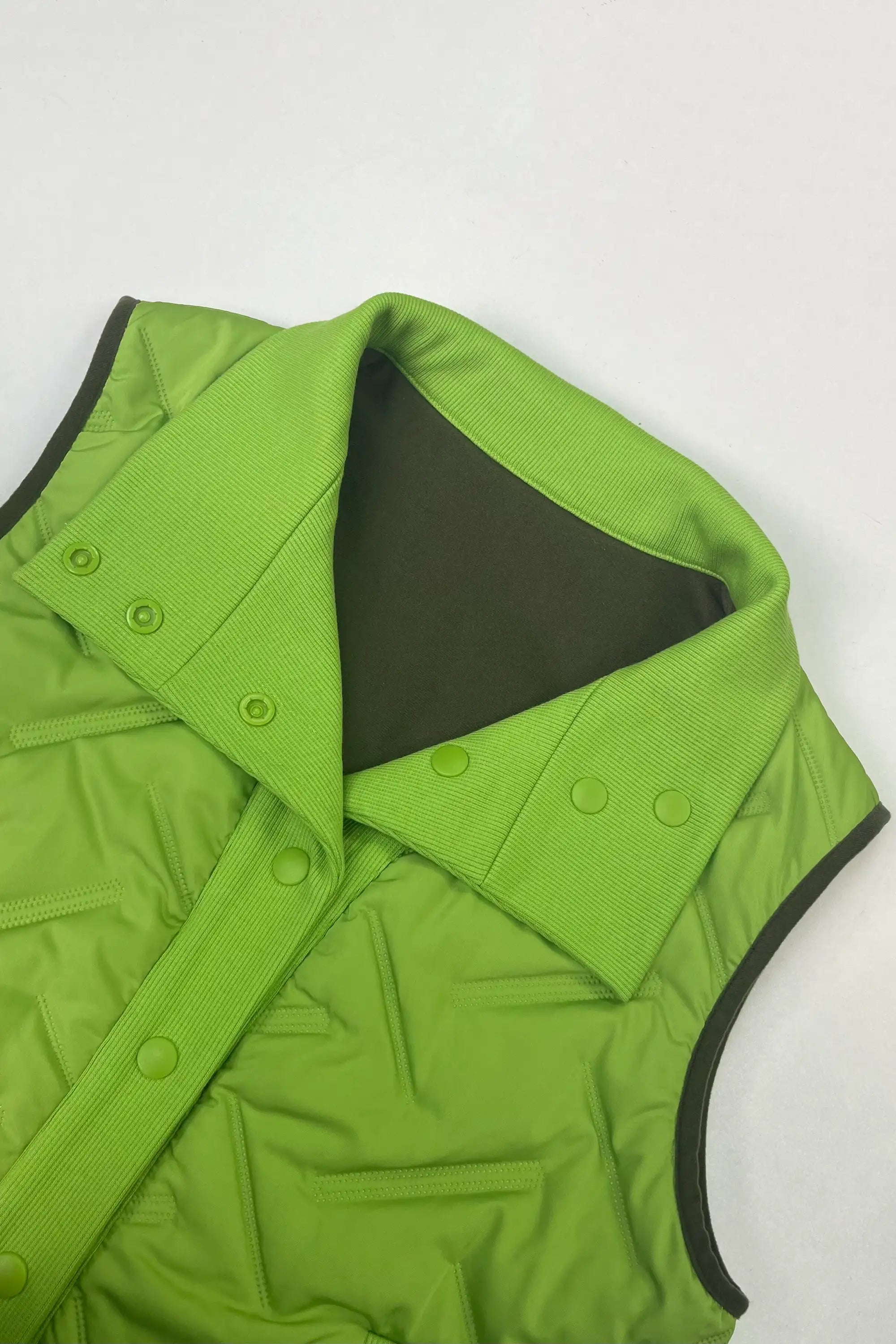 Close-up of reversible women’s lightweight puffer vest showing the dark reverse side with bright green ribbed placket and buttons