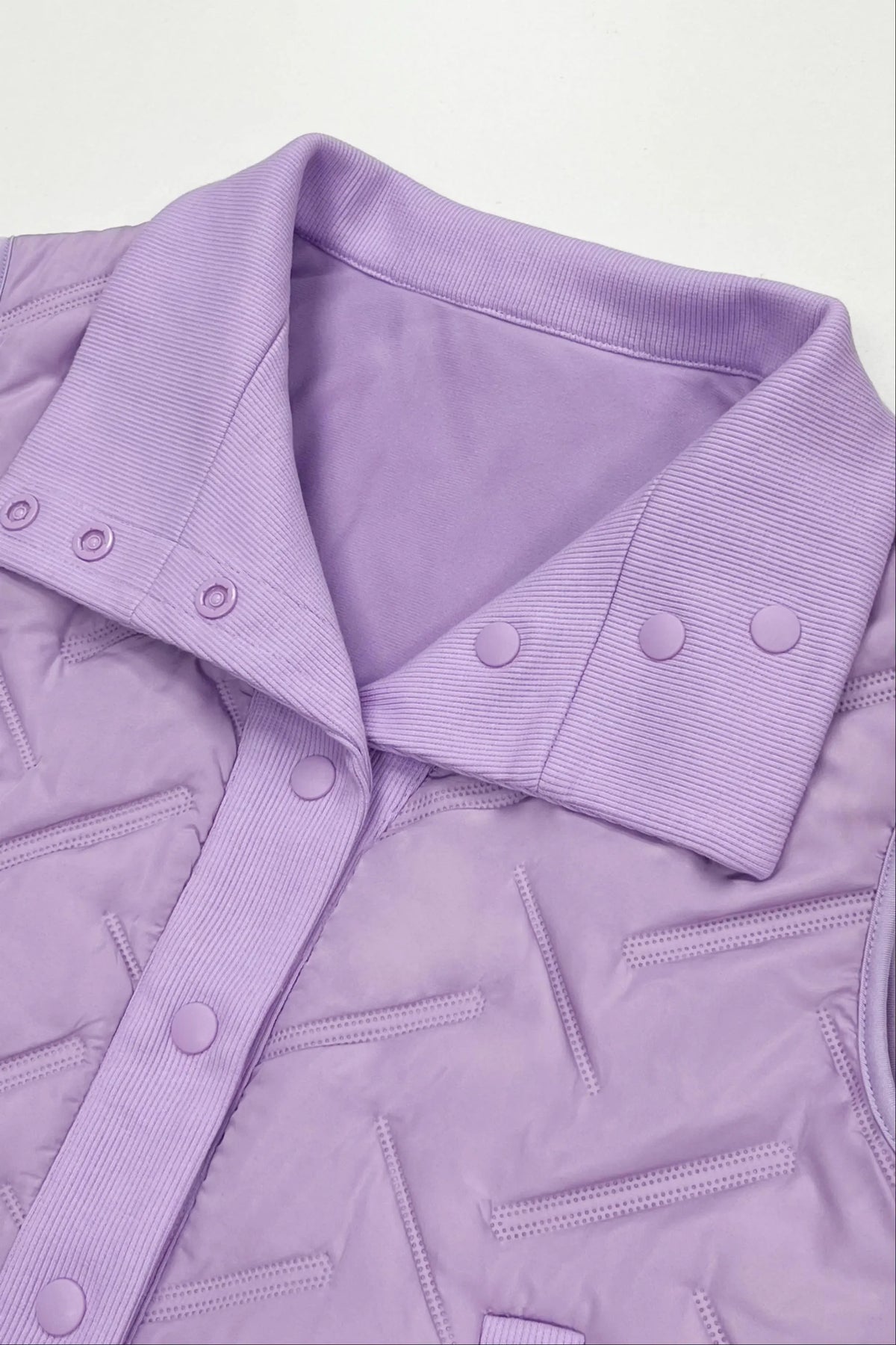 Close-up of women's lavender lightweight puffer vest showing the folded rib-knit collar, snap button details and quilted fabric