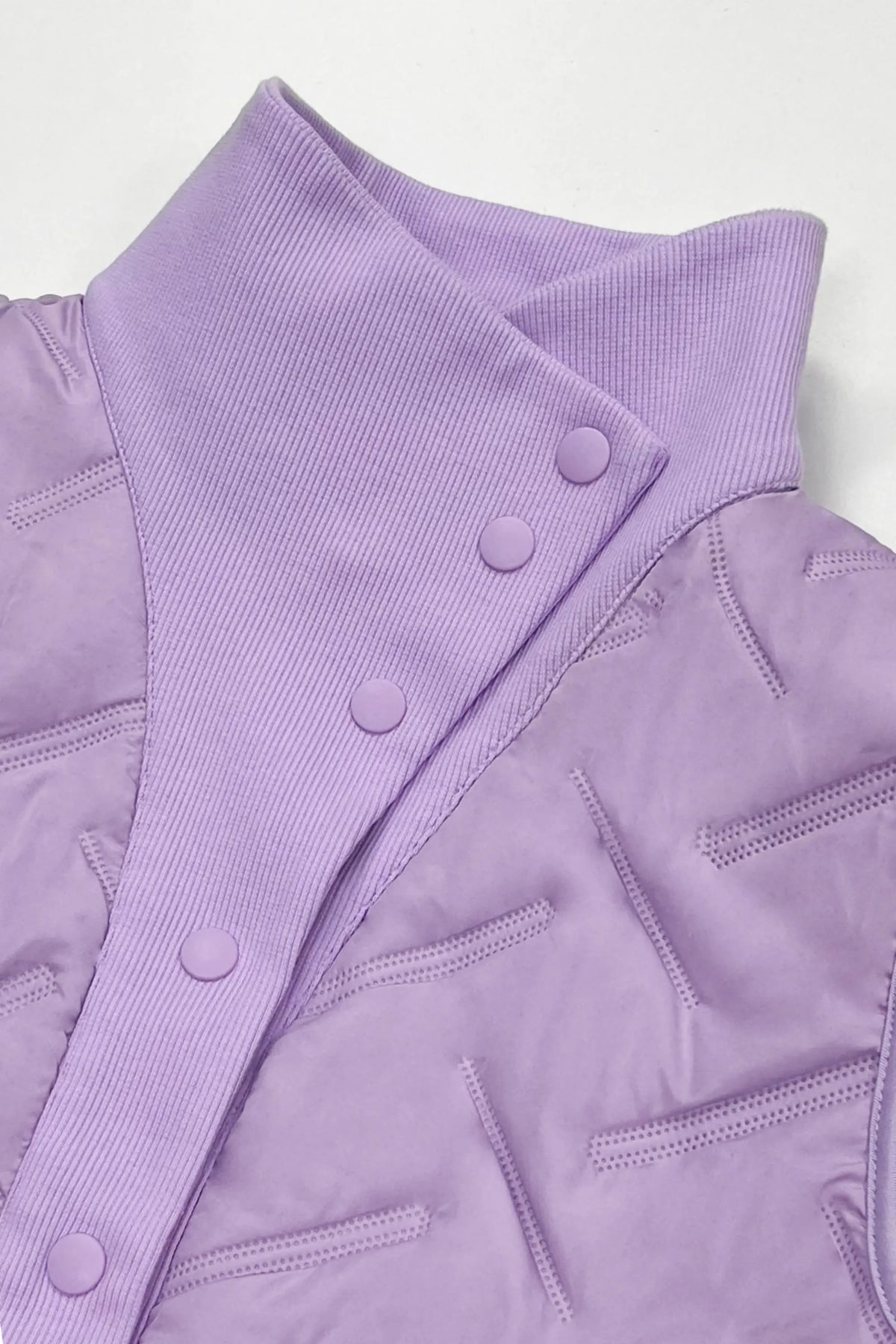 Close-up of women's lavender lightweight puffer vest showing the raised rib-knit collar, snap buttons and quilted fabric