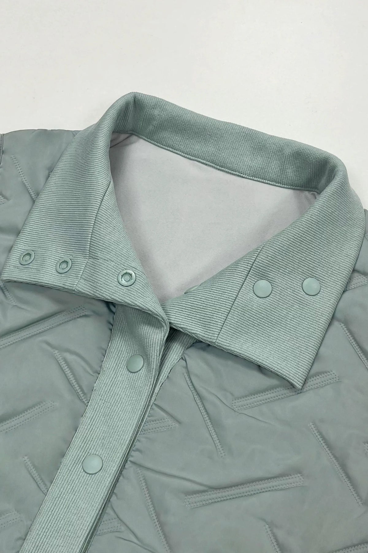 Close-up of women's sage grey lightweight puffer vest showing the folded rib-knit collar, button details and quilted fabric