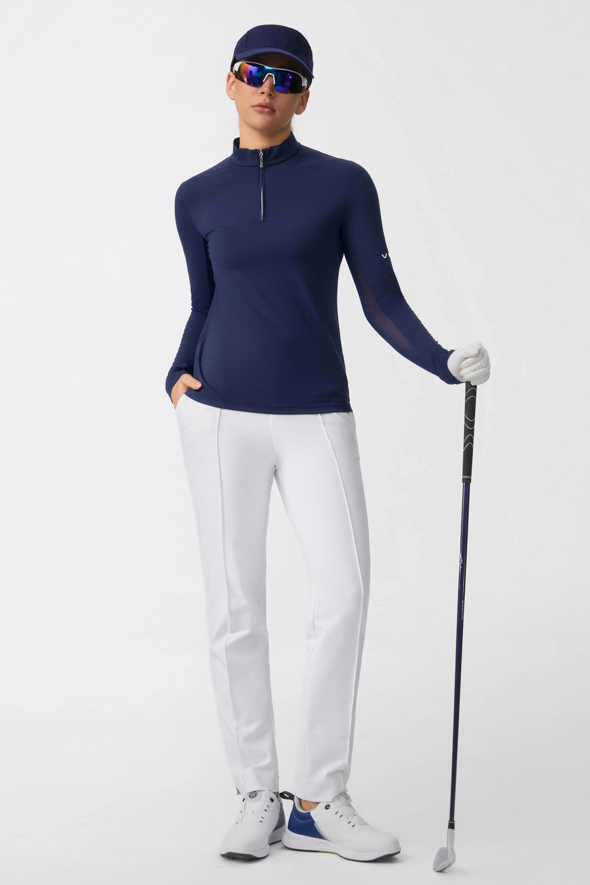 Women’s navy long sleeve zip neck golf top styled with white golf pants and golf club