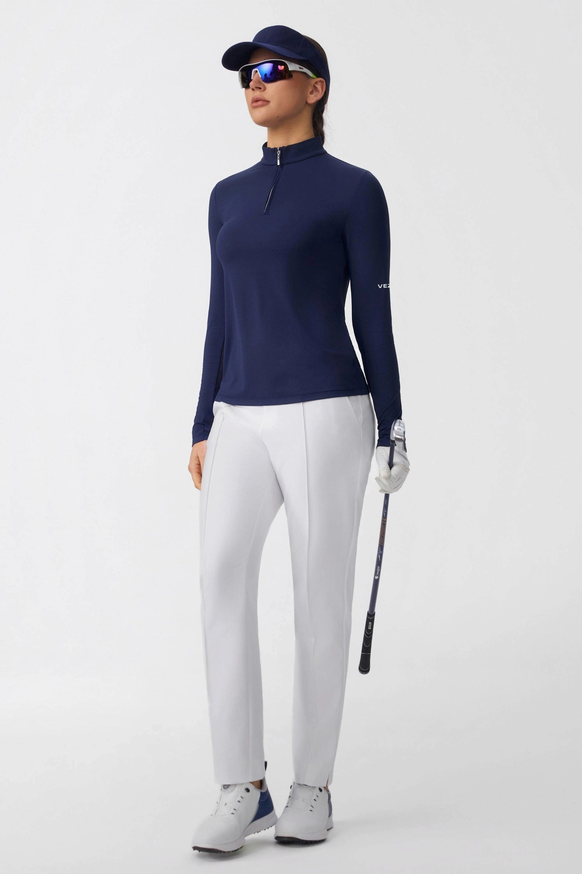 Navy long sleeve zip neck golf top worn by a golfer with white pants and visor
