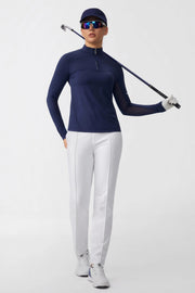 Women wearing a navy long sleeve zip neck golf top with white golf pants while holding a golf club