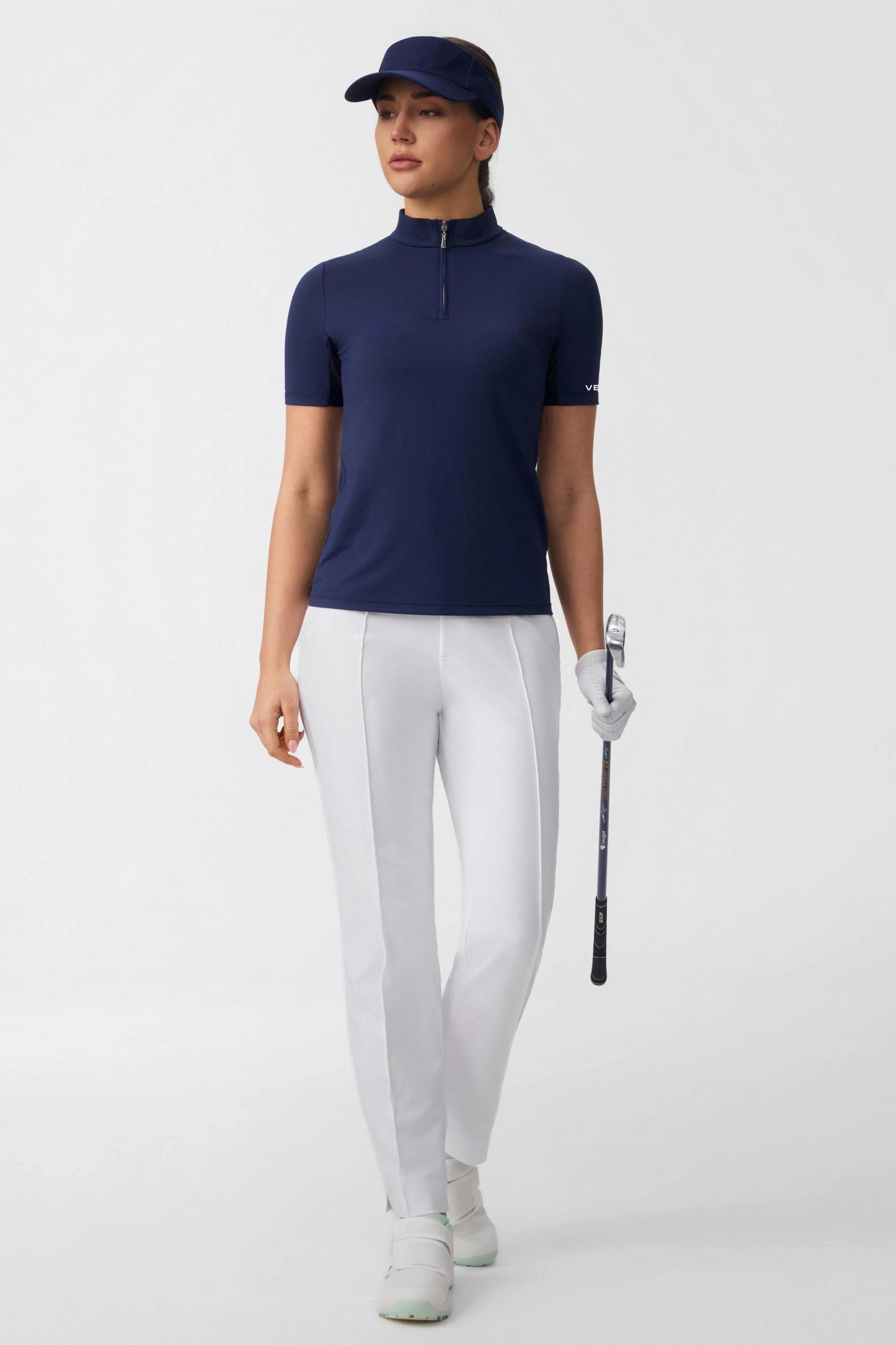 Model wearing a navy zip neck golf top styled with white golf pants for a clean golf outfit