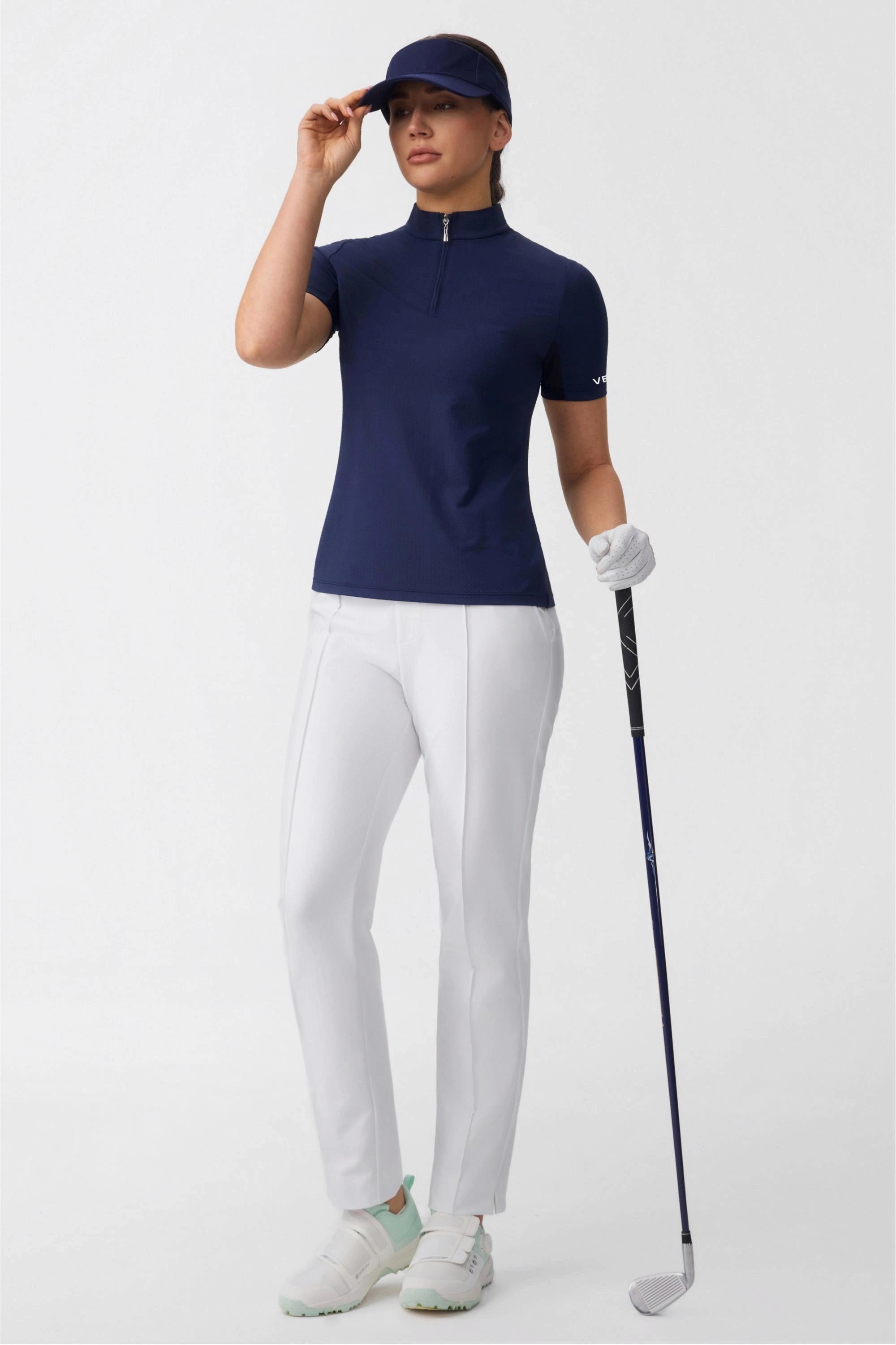 Model wearing a navy zip neck golf top with a visor and golf club for a modern golf look