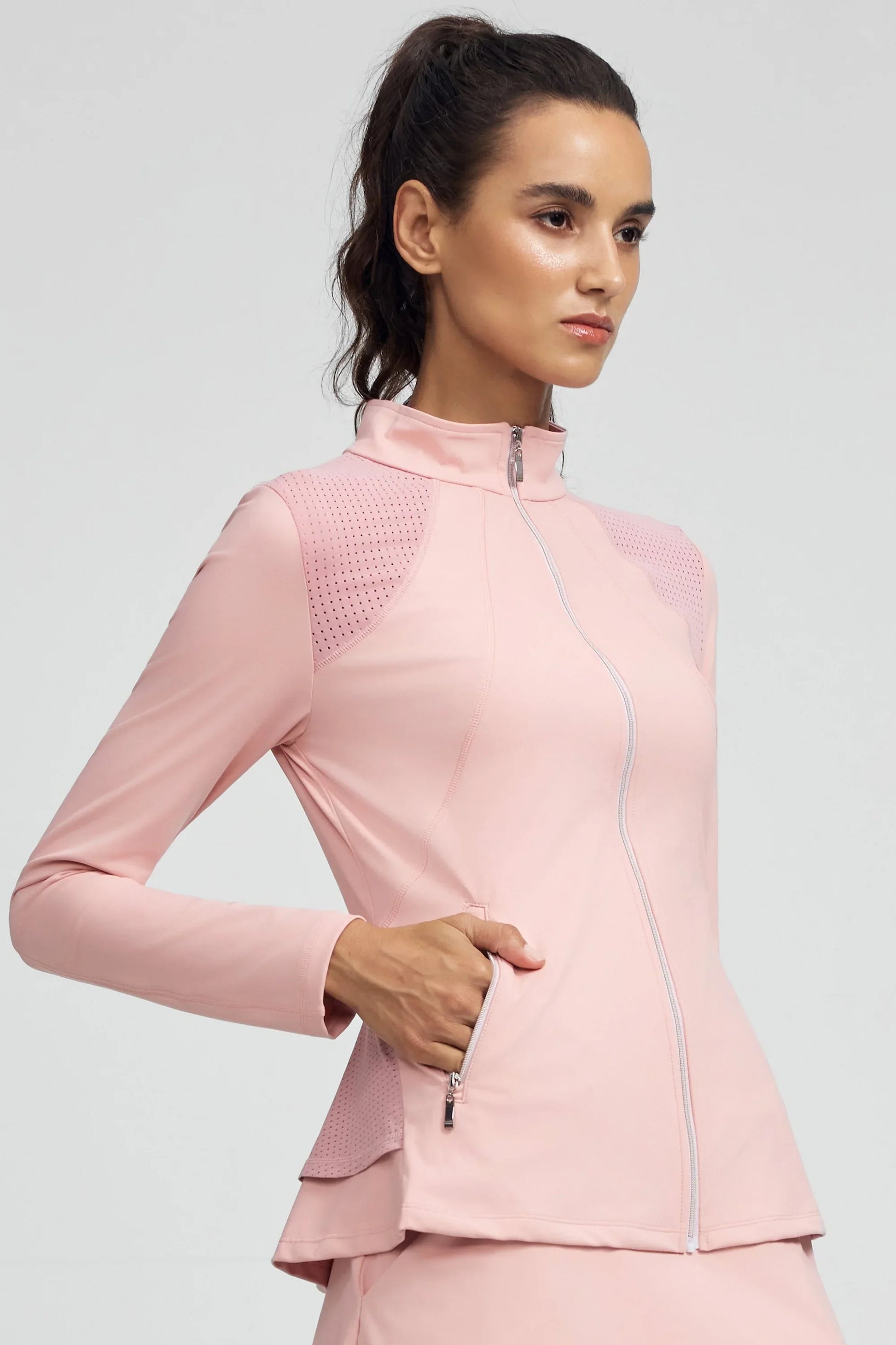 Side front view of women’s peplum zip golf jacket with mesh panels in pink showing the front zip, perforated shoulder panels, and zip pockets