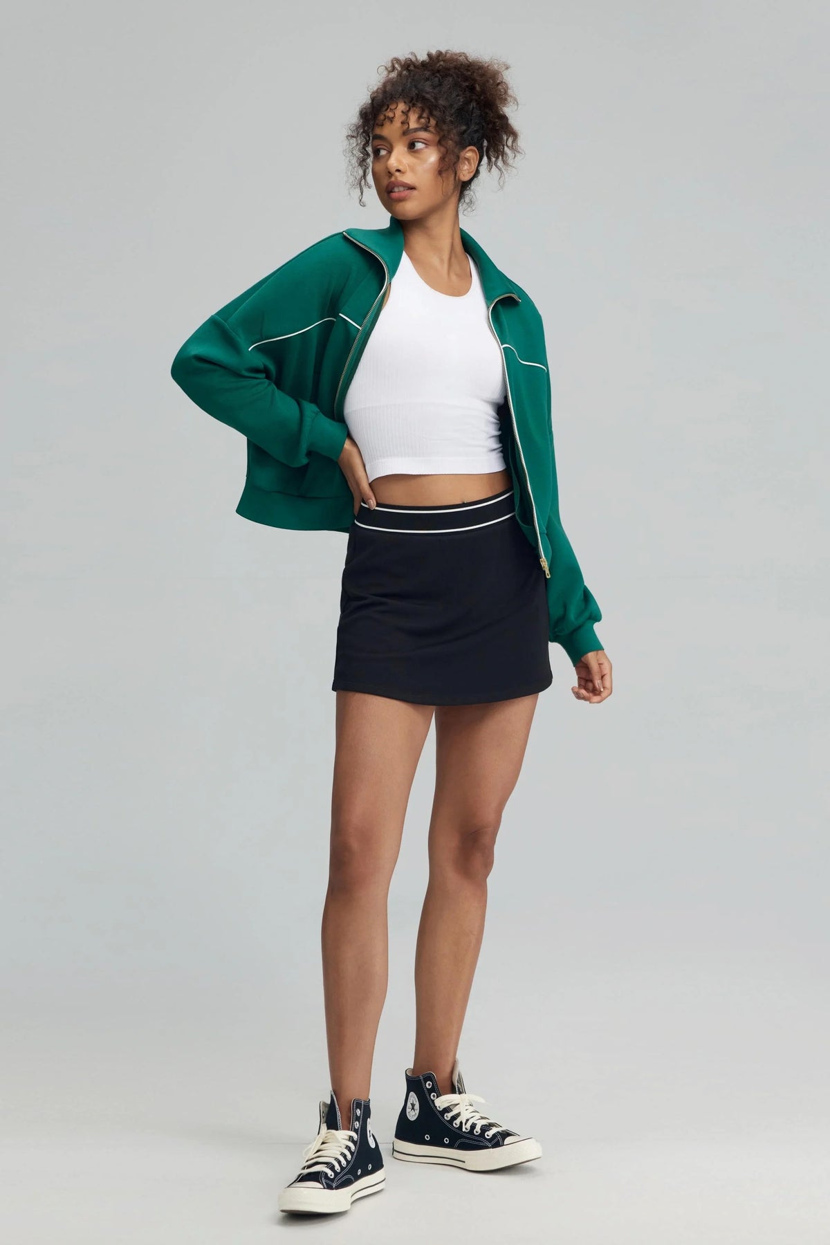 Women’s black performance golf skort styled with green zip jacket, front view