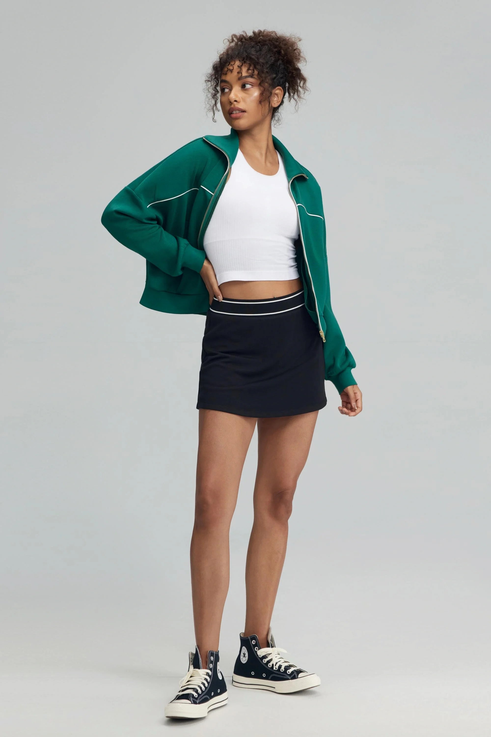 Women’s black performance golf skort styled with green zip jacket, front view