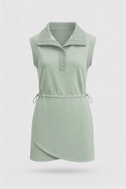 Front view of women's sage green sleeveless golf dress with folded collar, adjustable drawcord waist and asymmetric wrap hem