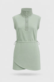 Front view of women's sage green sleeveless golf dress with buttoned stand collar, drawcord waist and asymmetric wrap hem