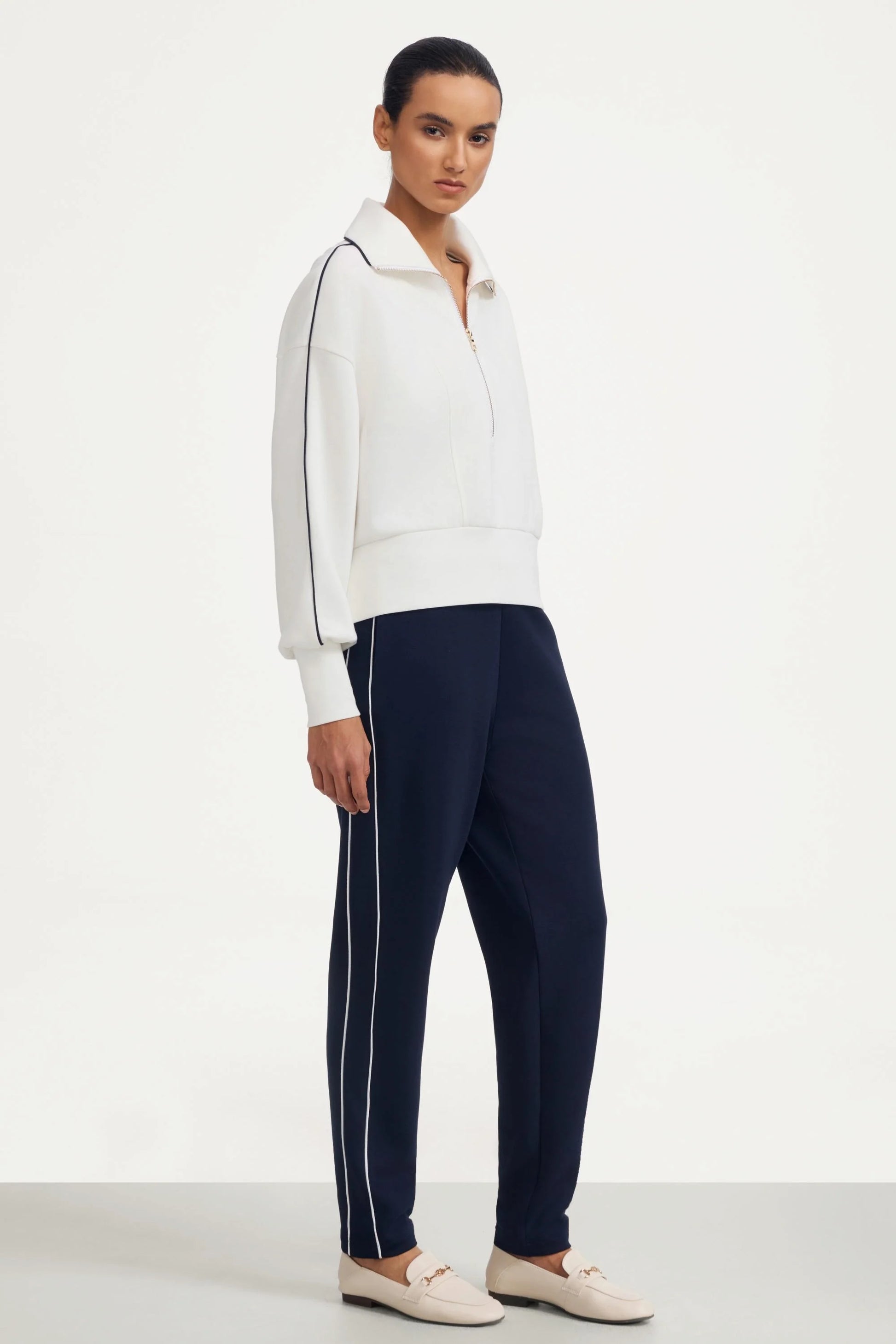 Side full-length view of a woman wearing a women’s half-zip golf pullover in ivory with navy golf pants