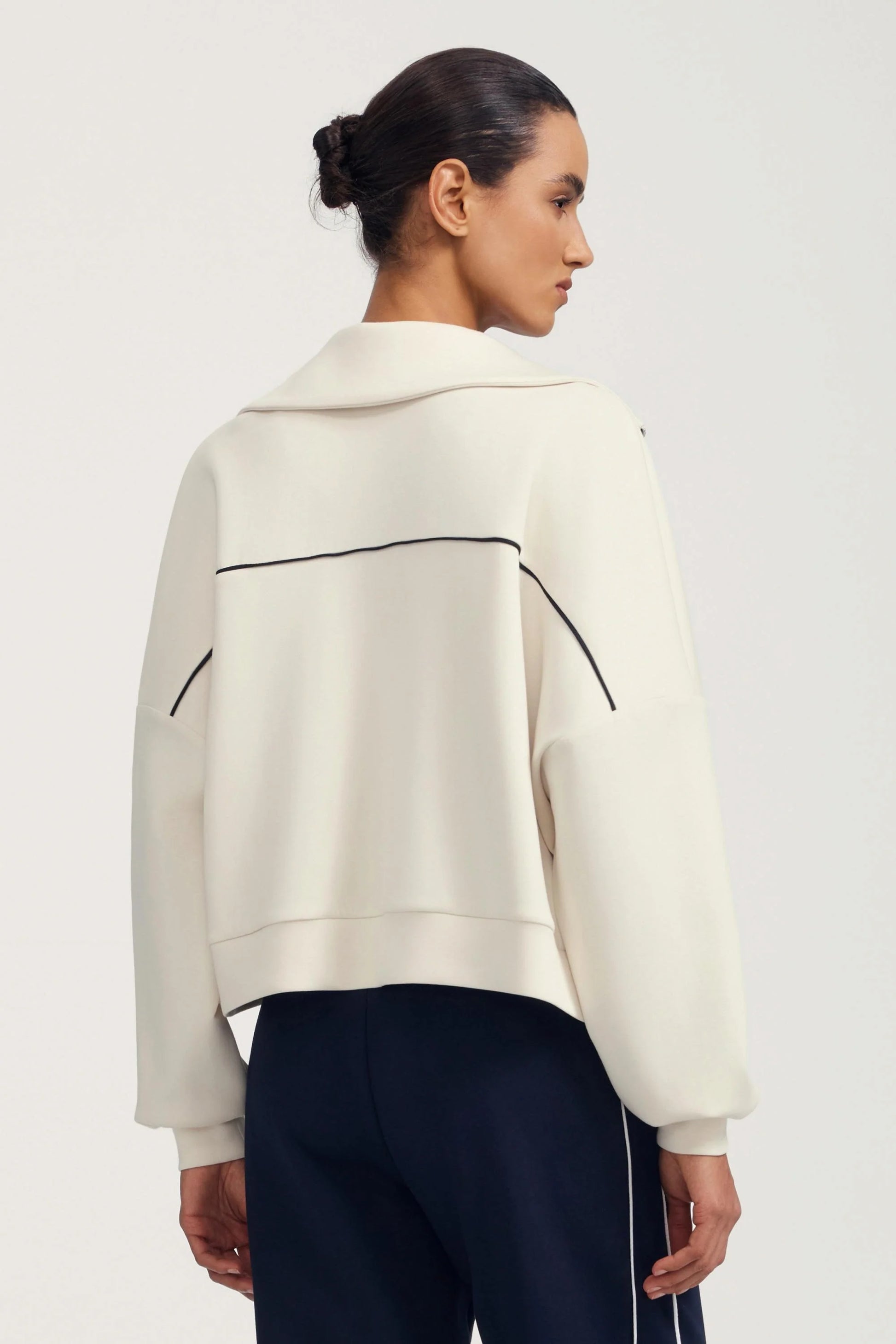 Back view of a women’s cream cropped golf jacket with contrast piping detail