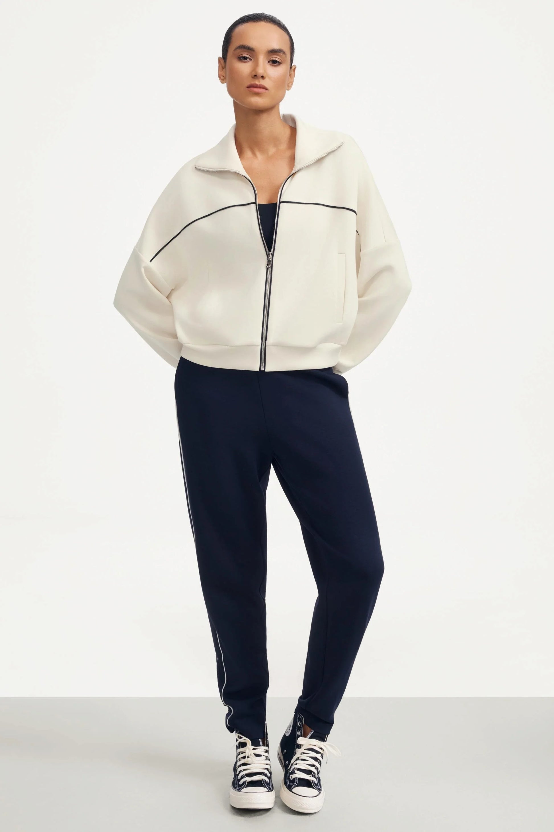 Front outfit view of a women’s cropped golf jacket in soft ivory styled with navy slim pants