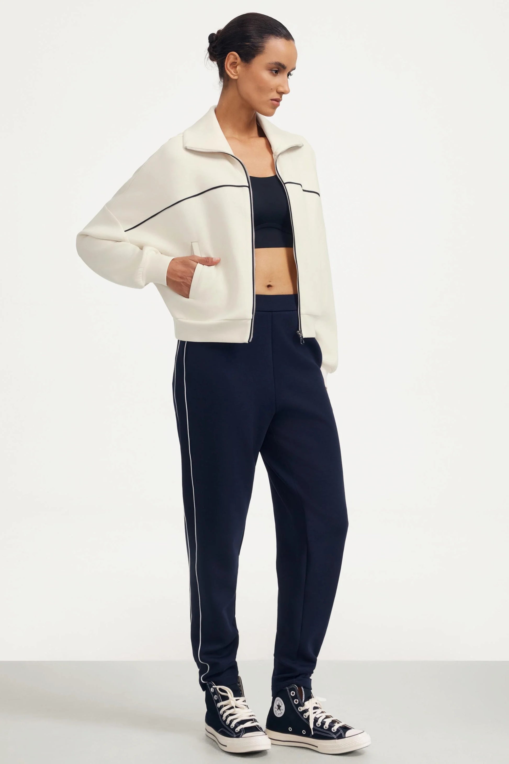 Woman wearing a white cropped golf jacket with navy track pants and sneakers