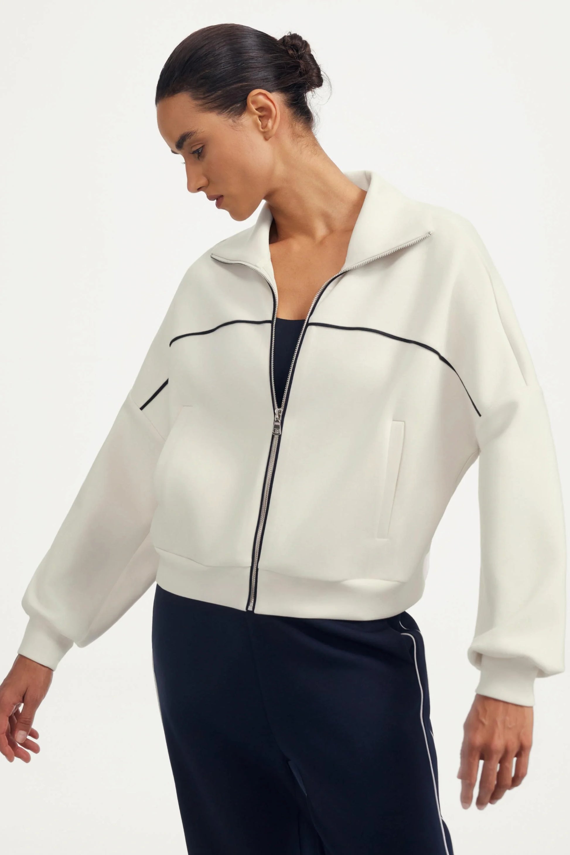 Side view of a women’s white cropped golf jacket with contrast piping and a zip-front neckline