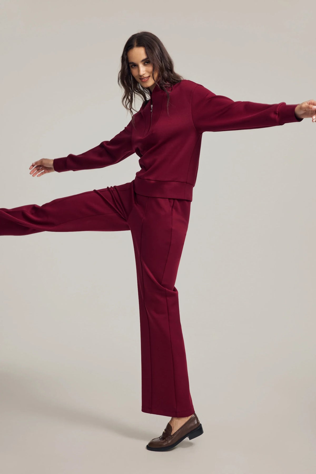 Woman balancing with arms extended in burgundy straight-leg pants and a coordinated pullover