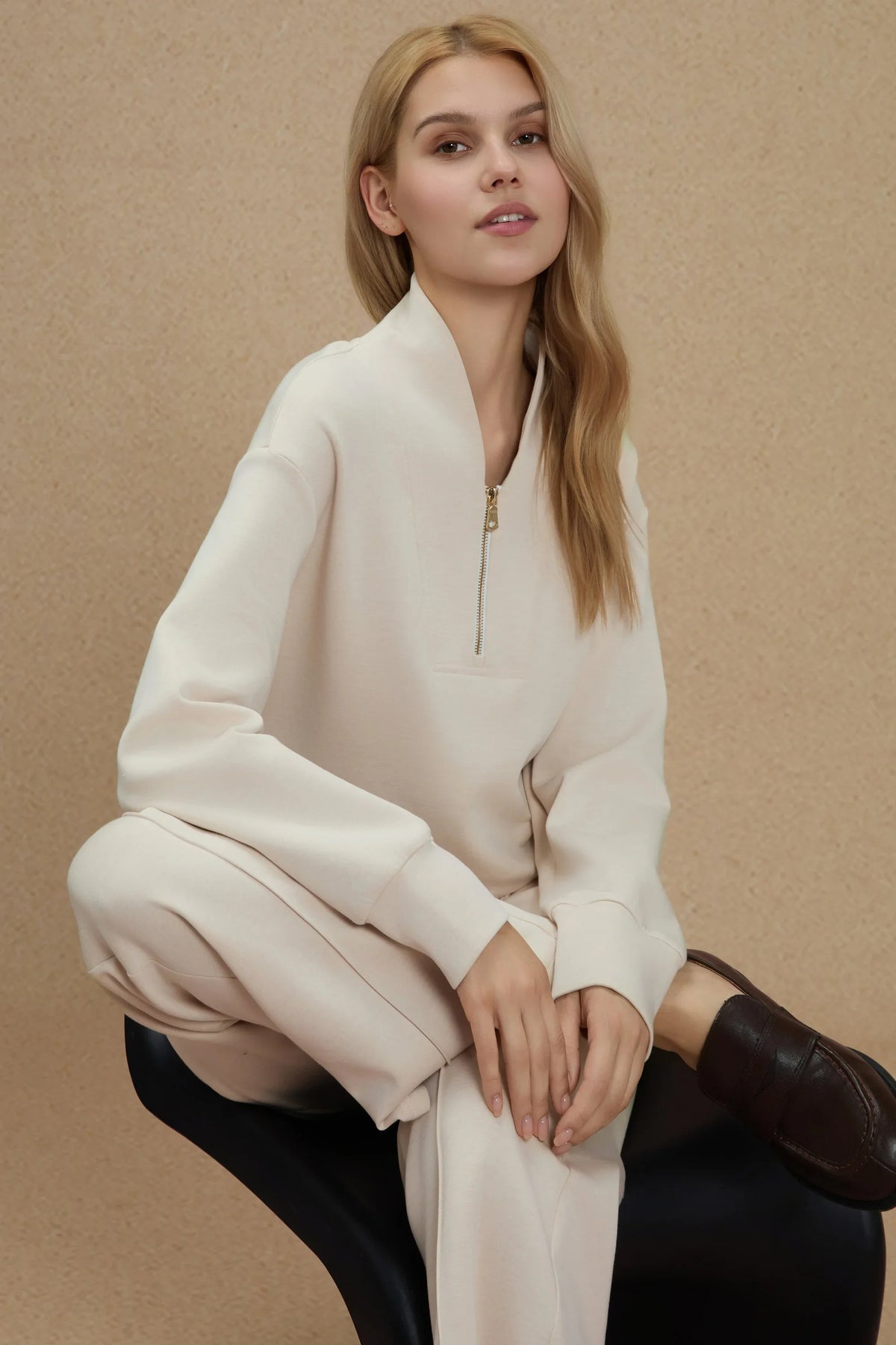 Woman seated in a coordinated Oatmilk outfit featuring relaxed straight-leg pants and a matching pullover