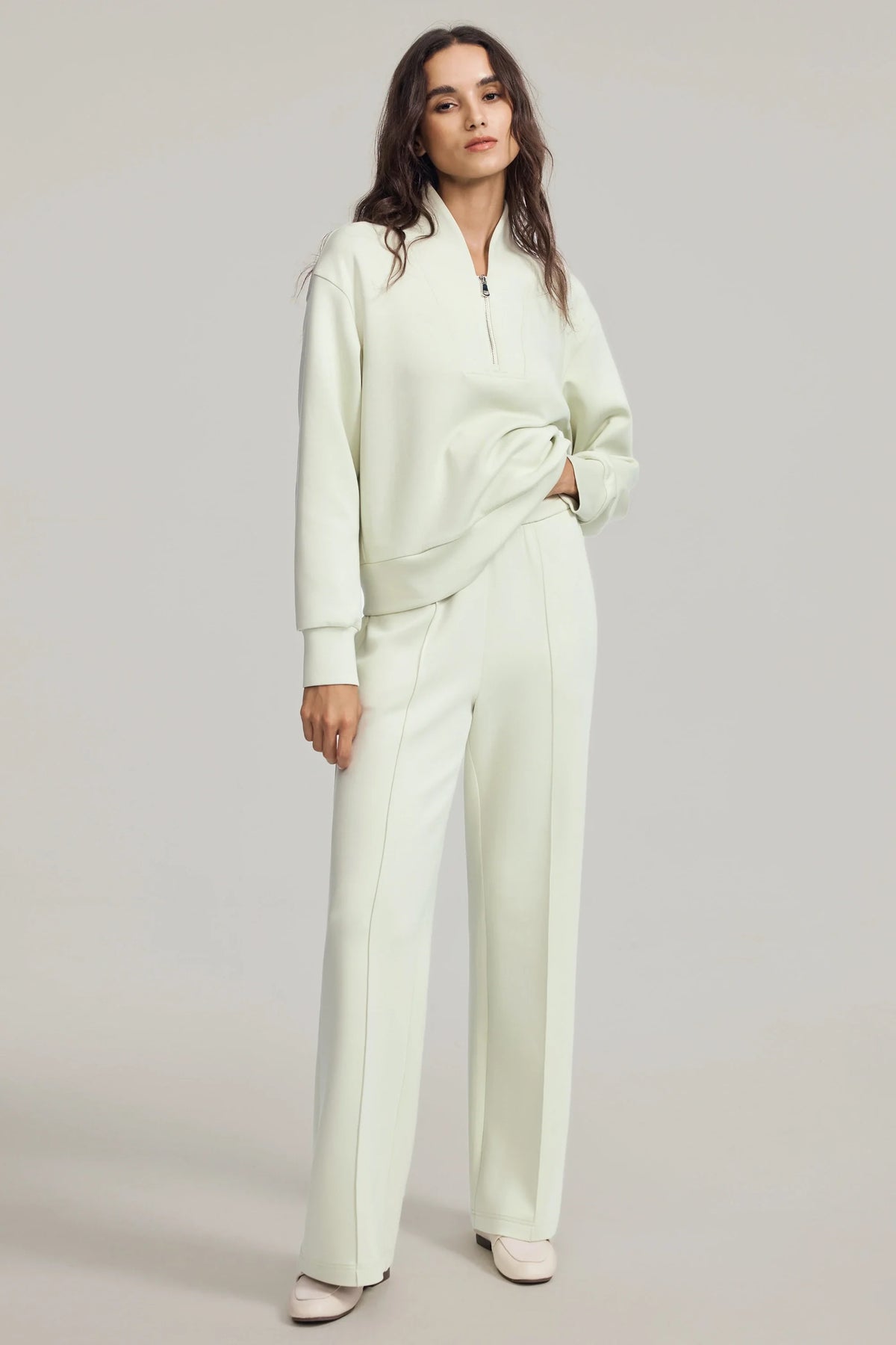 Woman wearing Pistachio Cream straight-leg pants with a matching half-zip pullover, showing the relaxed silhouette