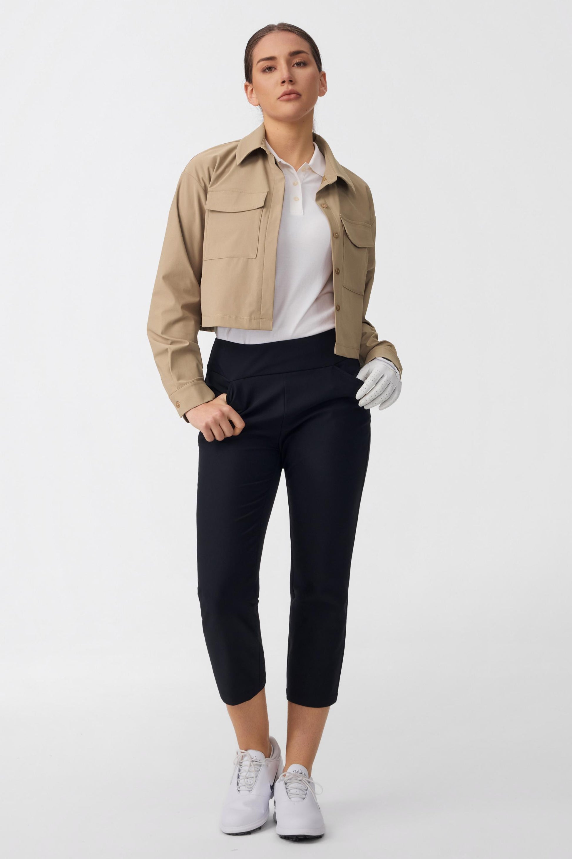 Women wearing onyx black tailored capri golf pants styled with a cropped golf jacket and white polo
