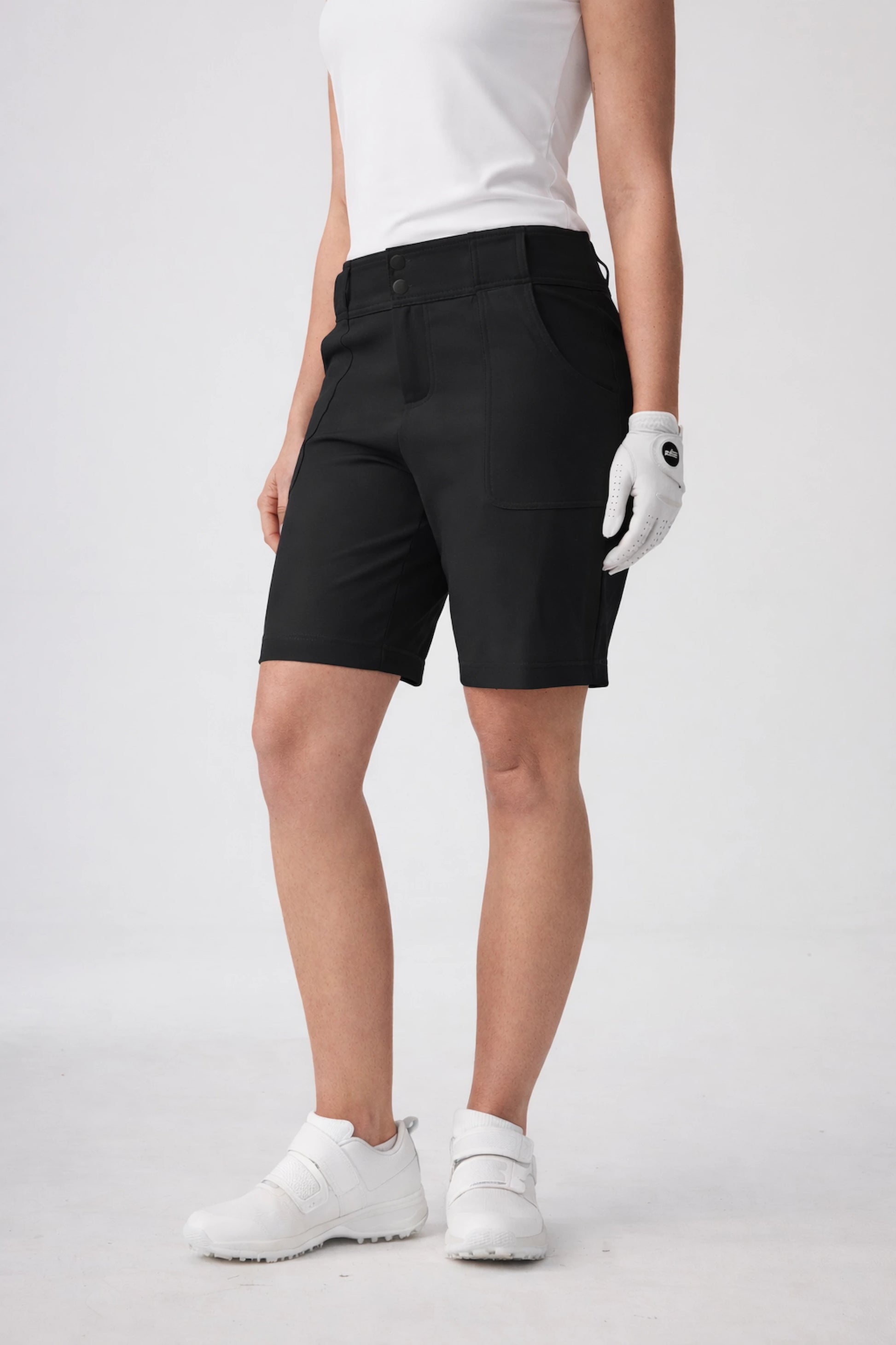 Side front view of model wearing women’s tailored utility bermuda golf shorts in black with a tailored fit and knee-length silhouette