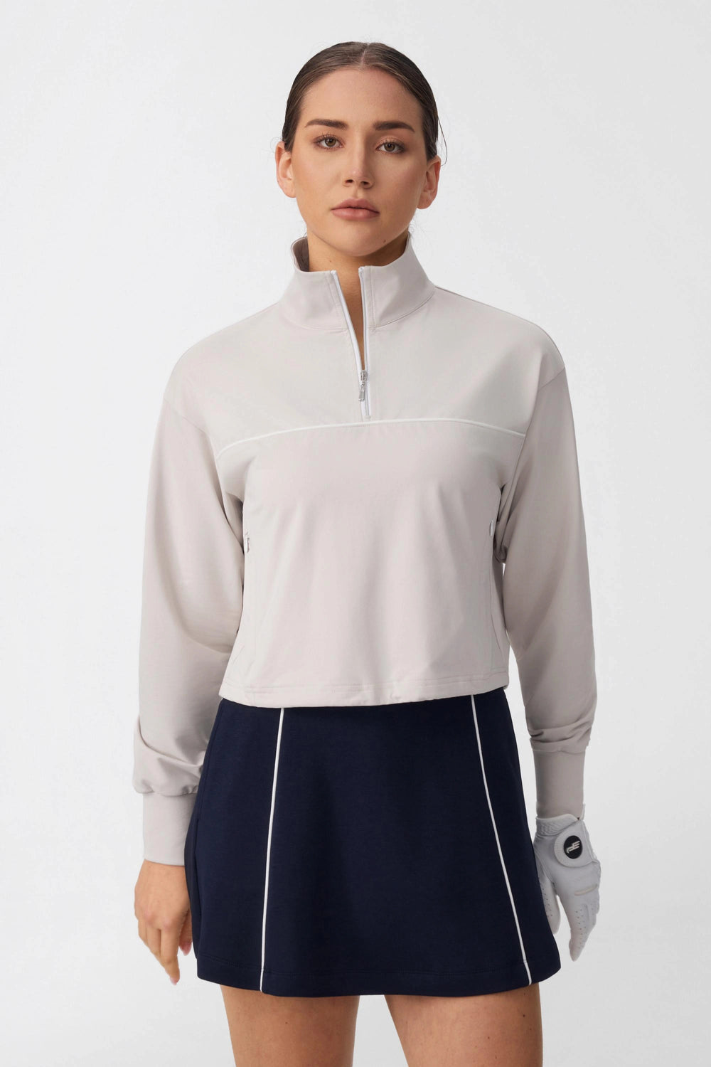 Woman wearing a soft taupe half-zip golf top with long sleeves and contrast piping