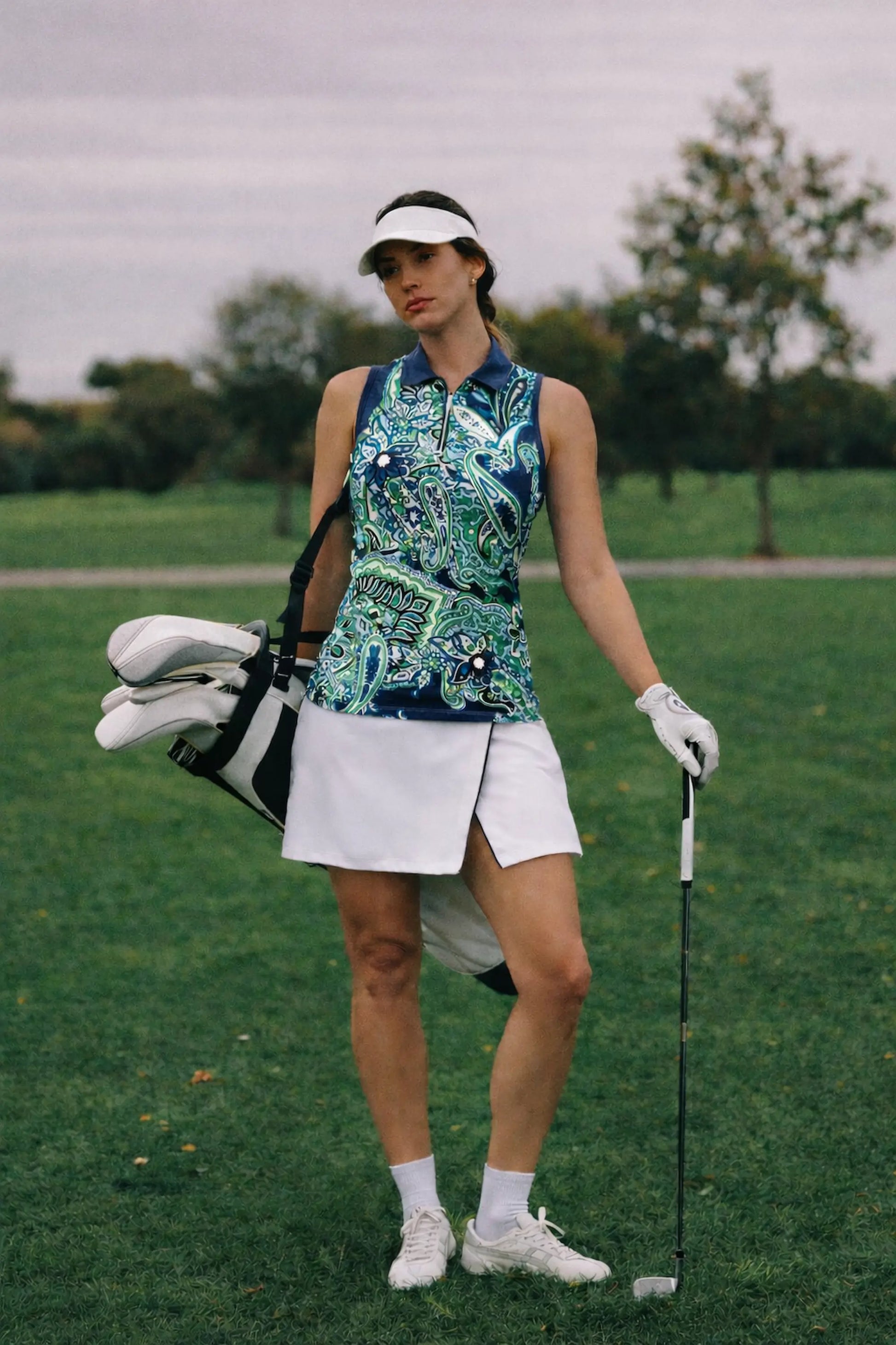 Woman wearing a crisp white wrap front golf skort on a golf course with a sleeveless patterned golf top
