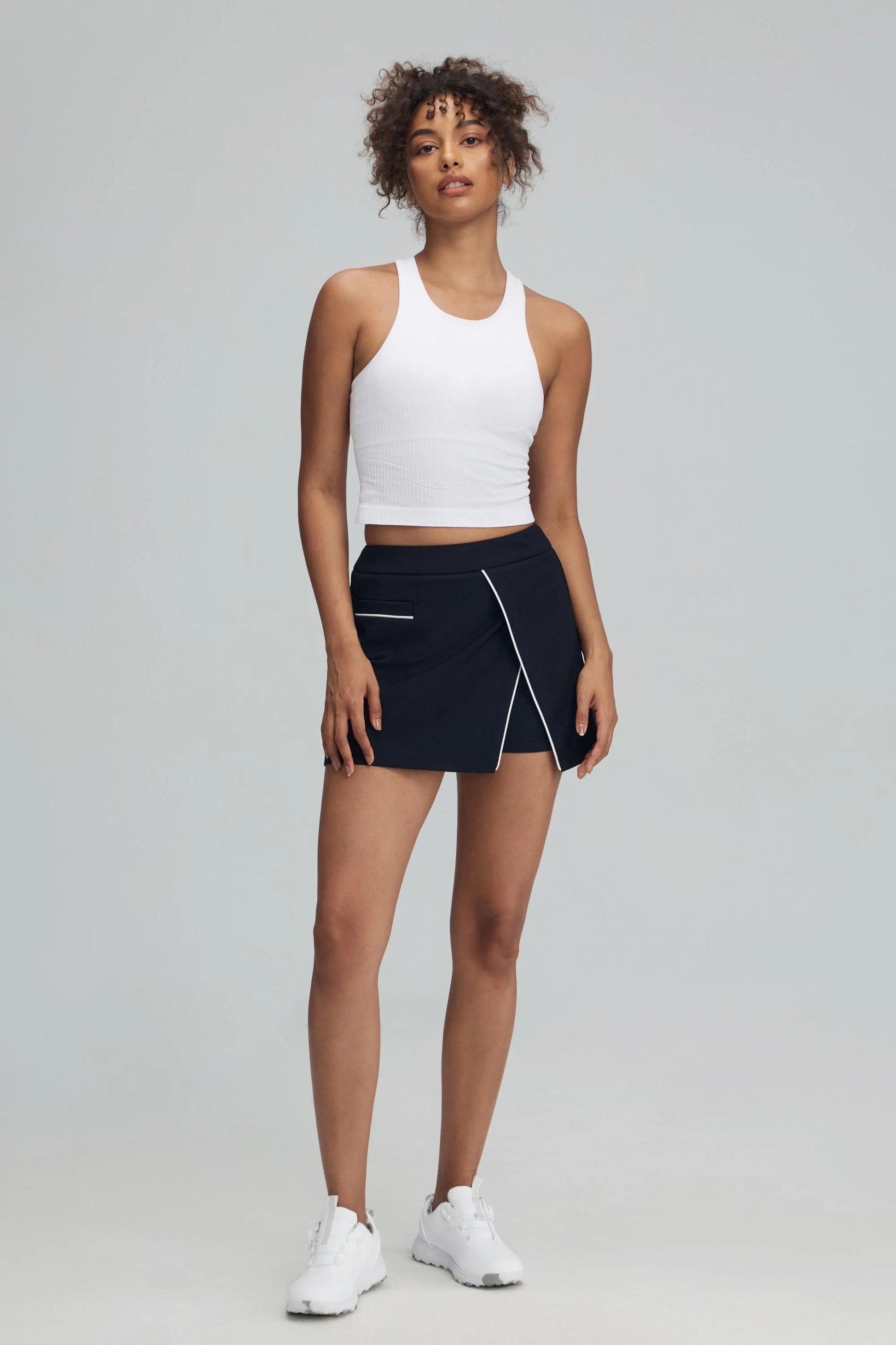 Women’s jet black wrap front golf skort with contrast piping styled with a white athletic tank