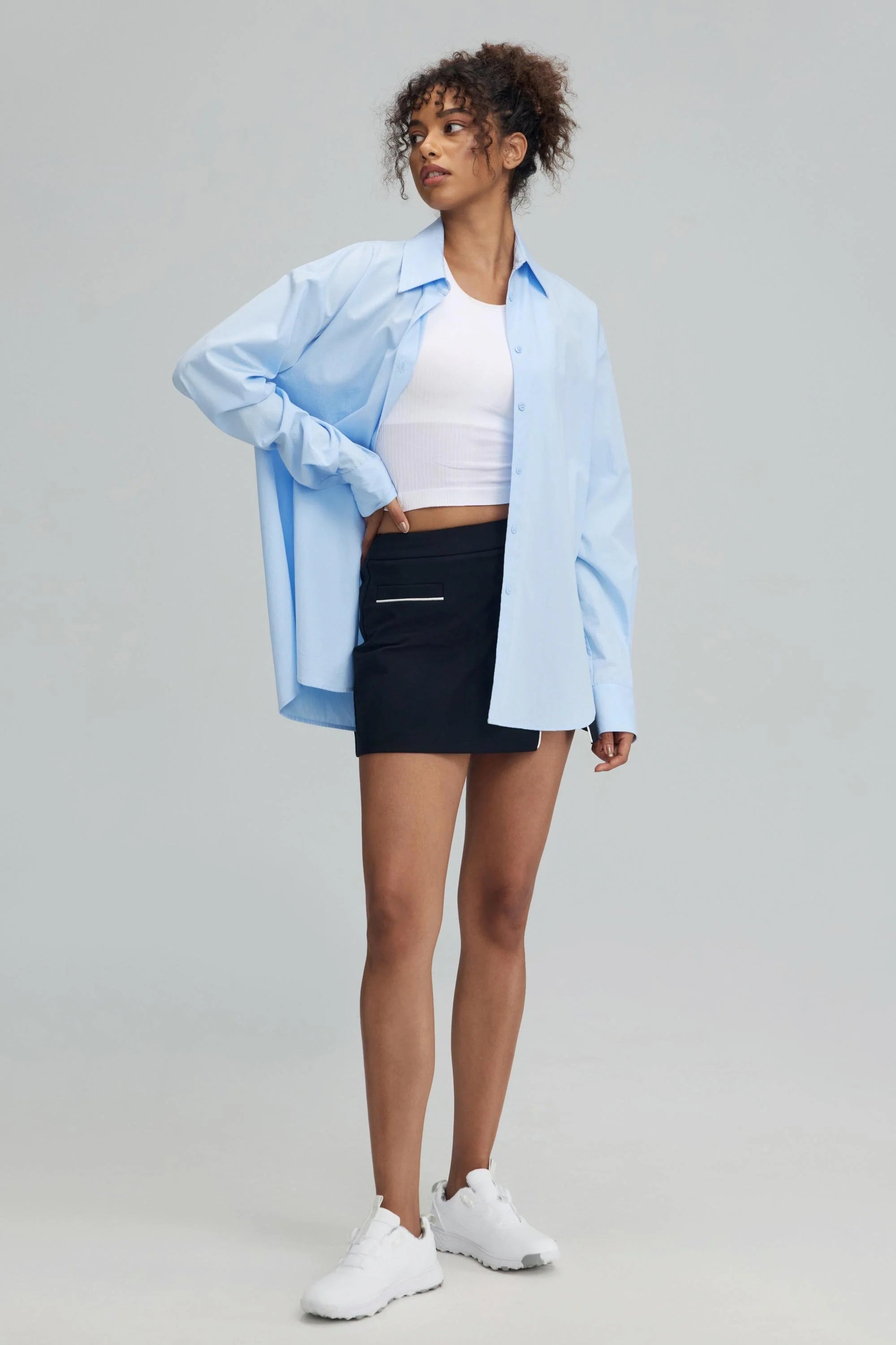 Women’s jet black wrap front golf skort styled with a white tank and light blue button-down shirt