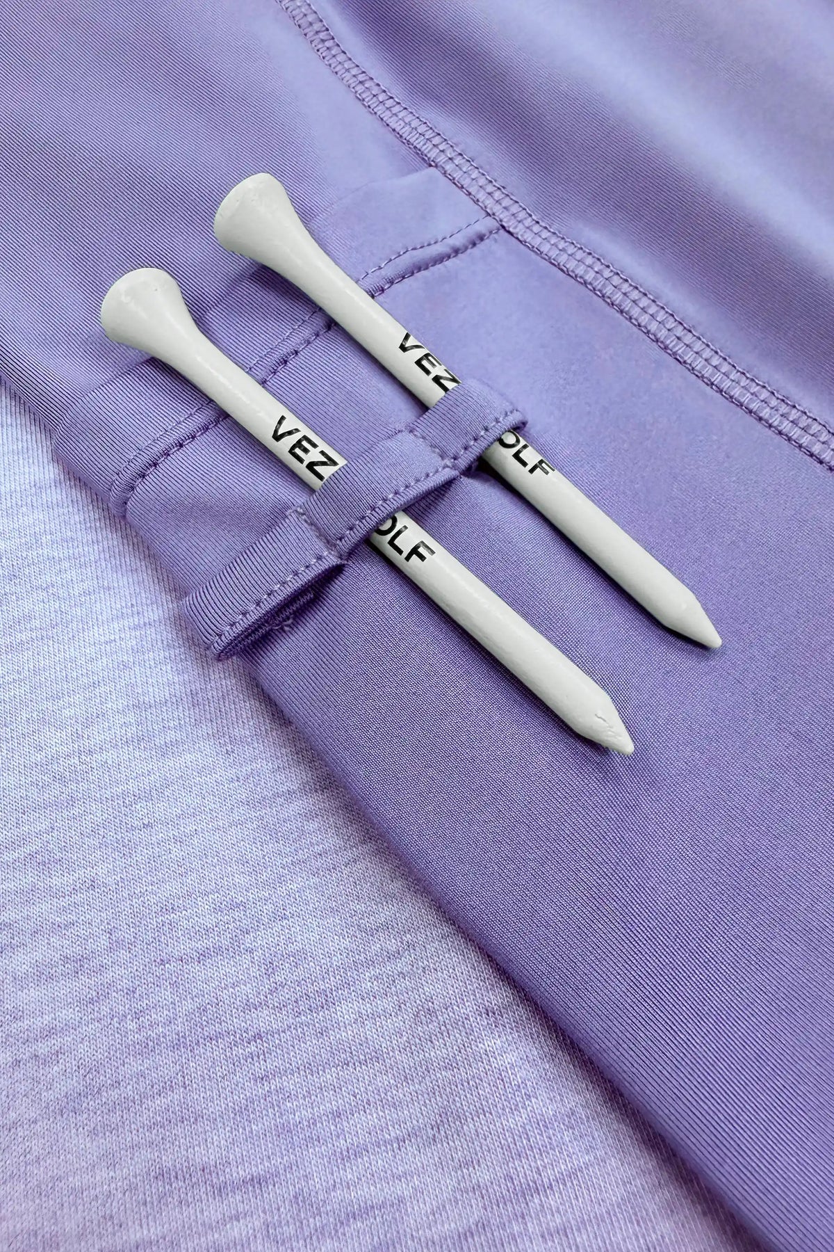Close-up of the built-in shorts with fabric loops holding two white golf tees on the lavender golf skort