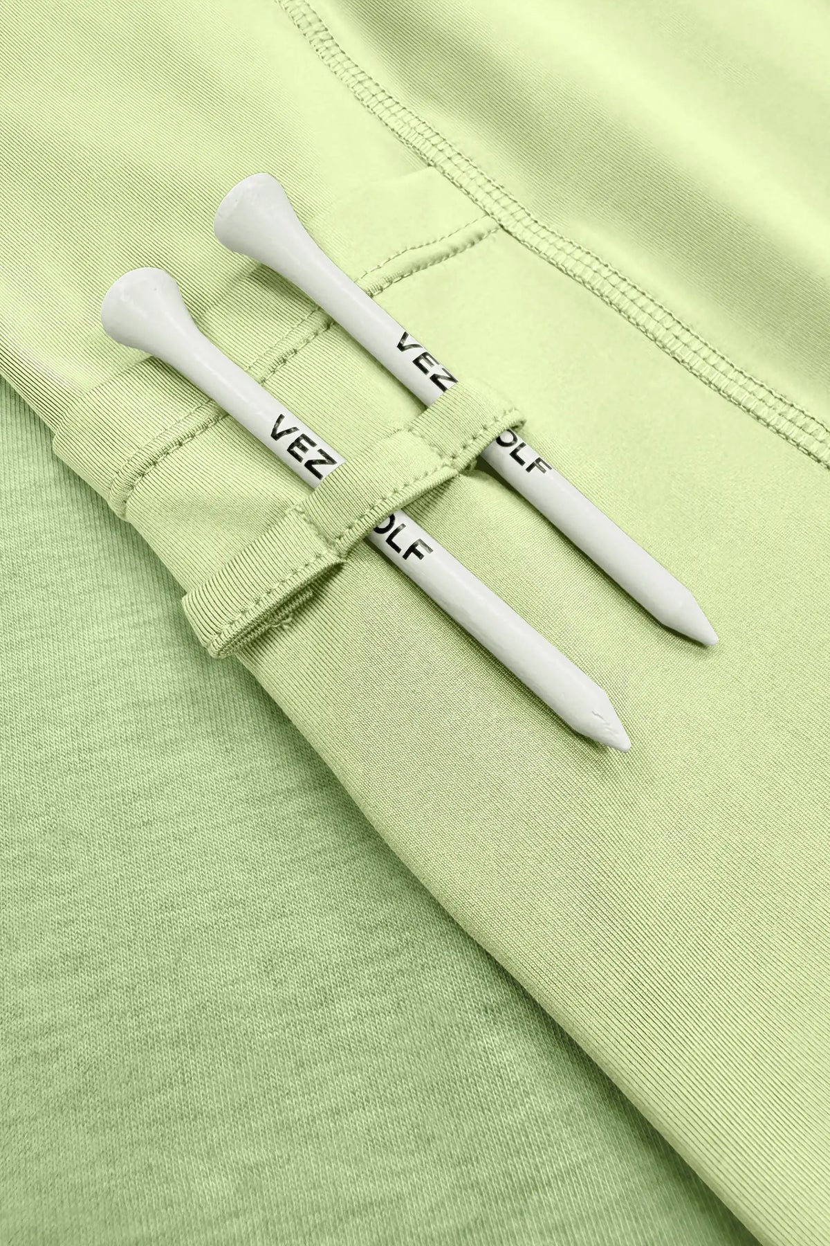 Close-up of the built-in shorts with fabric loops holding two white golf tees on the light green golf skort