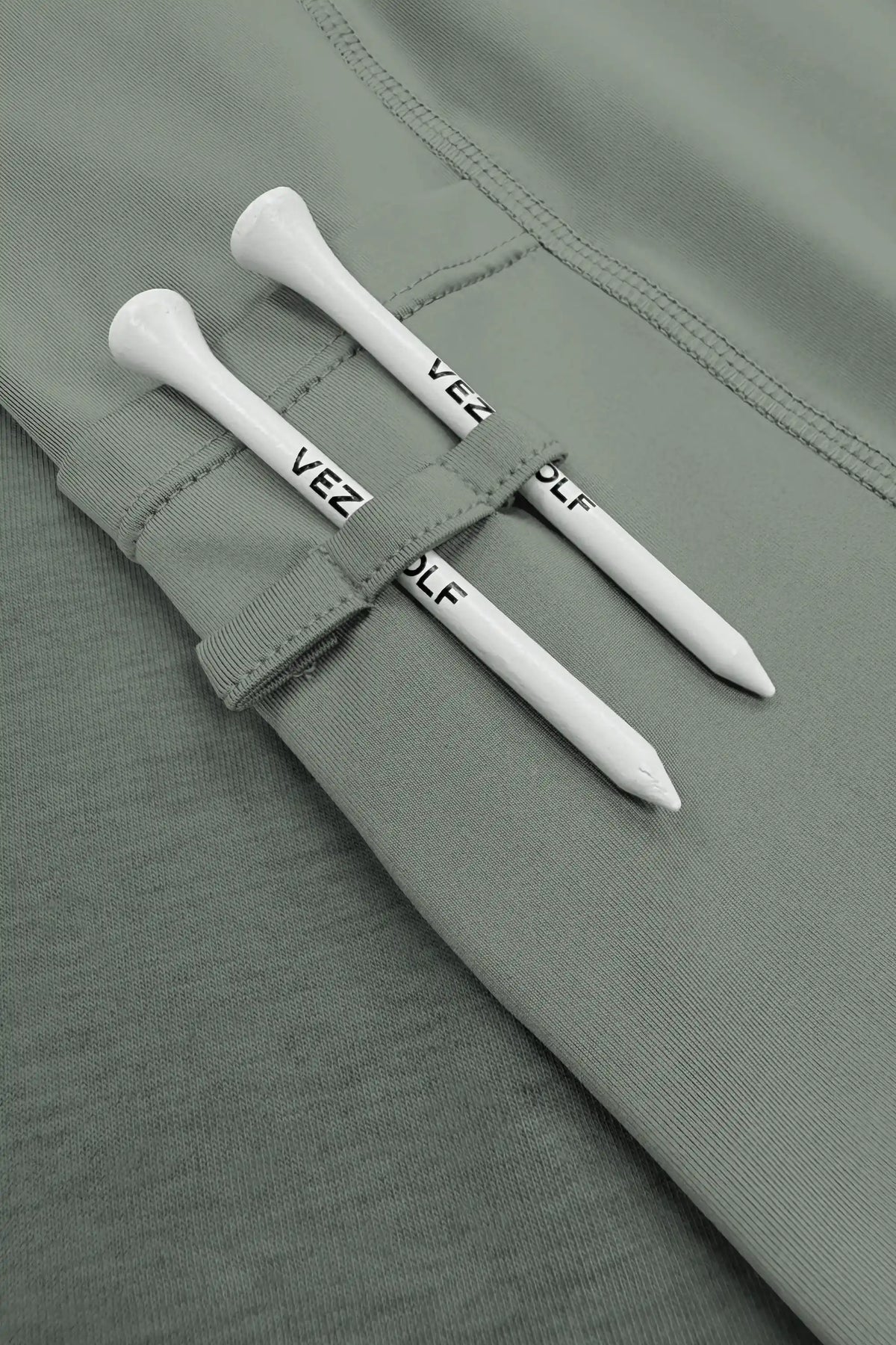 Close-up of the built-in shorts with fabric loops holding two white golf tees on the grey-green golf skort