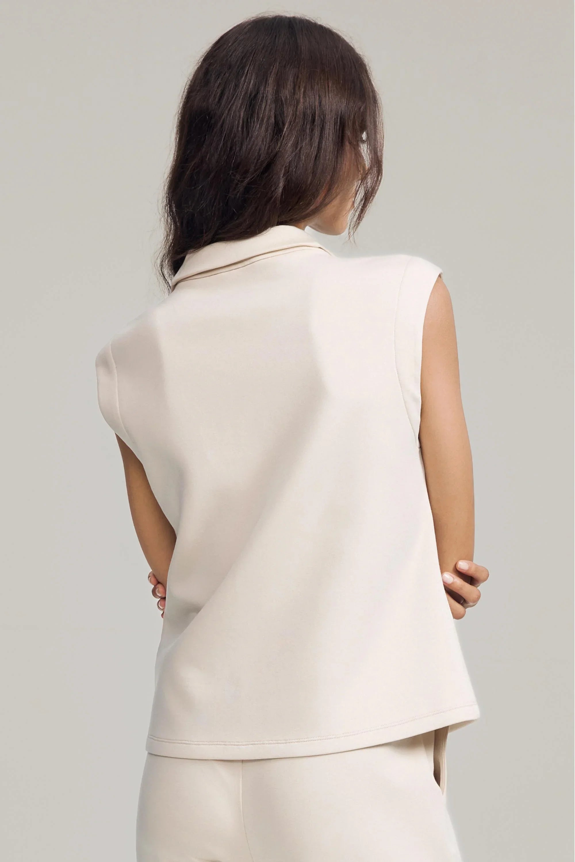 Back view of women’s cream sleeveless pullover with clean minimalist silhouette
