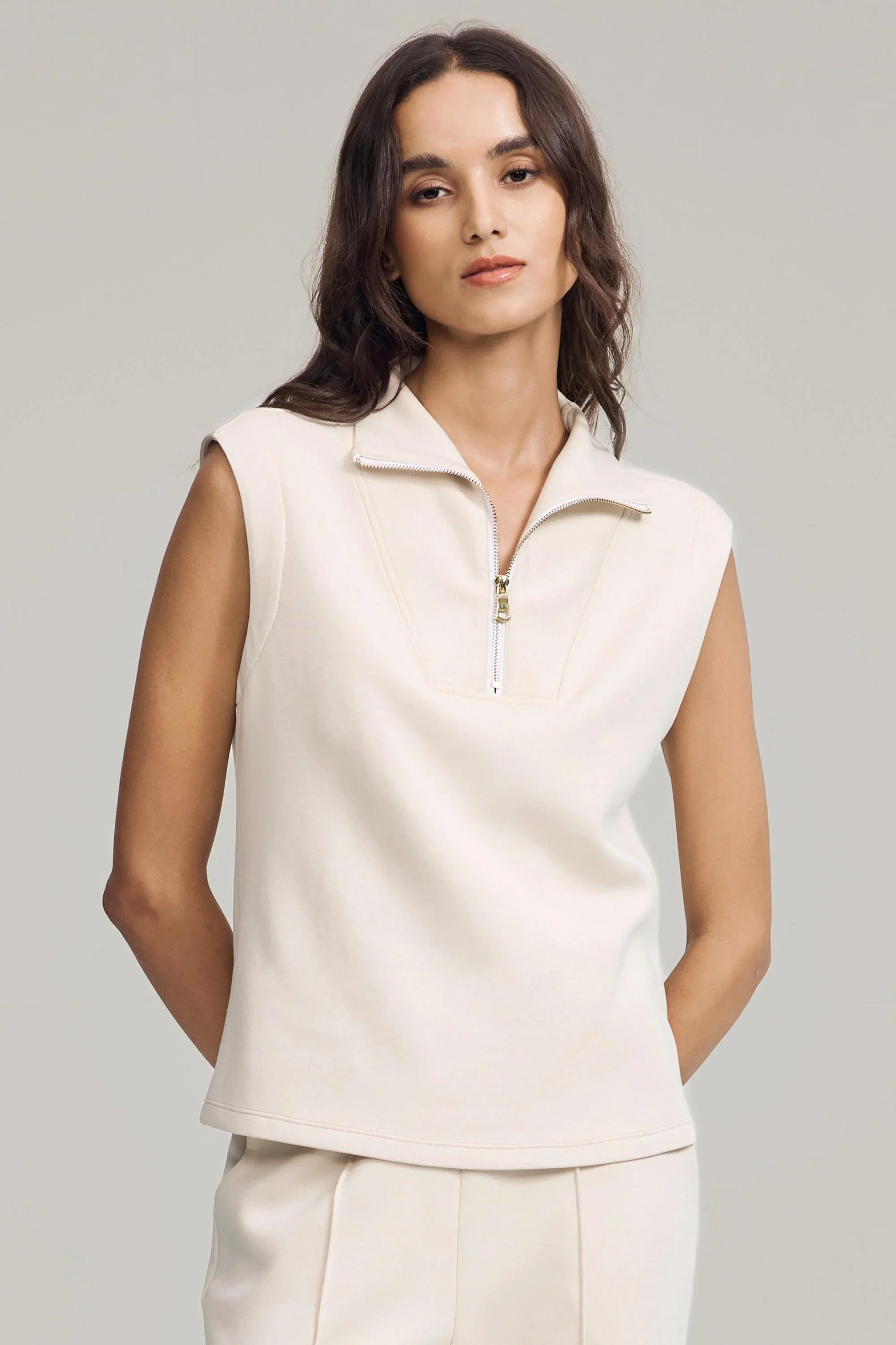 Women’s cream sleeveless pullover featuring structured collar and gold zip detail