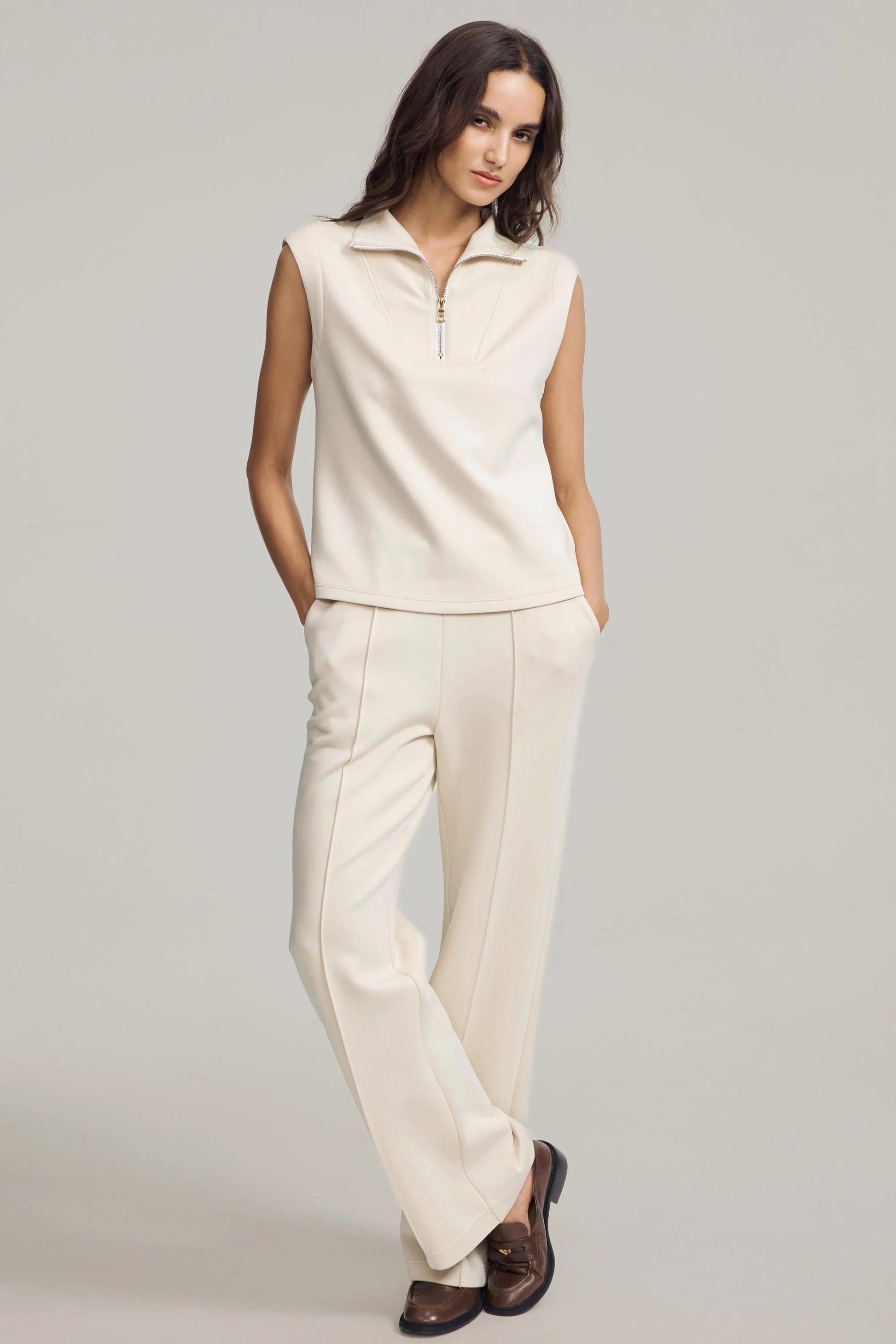 Women’s sleeveless zip-collar pullover in cream styled with wide-leg pants and loafers